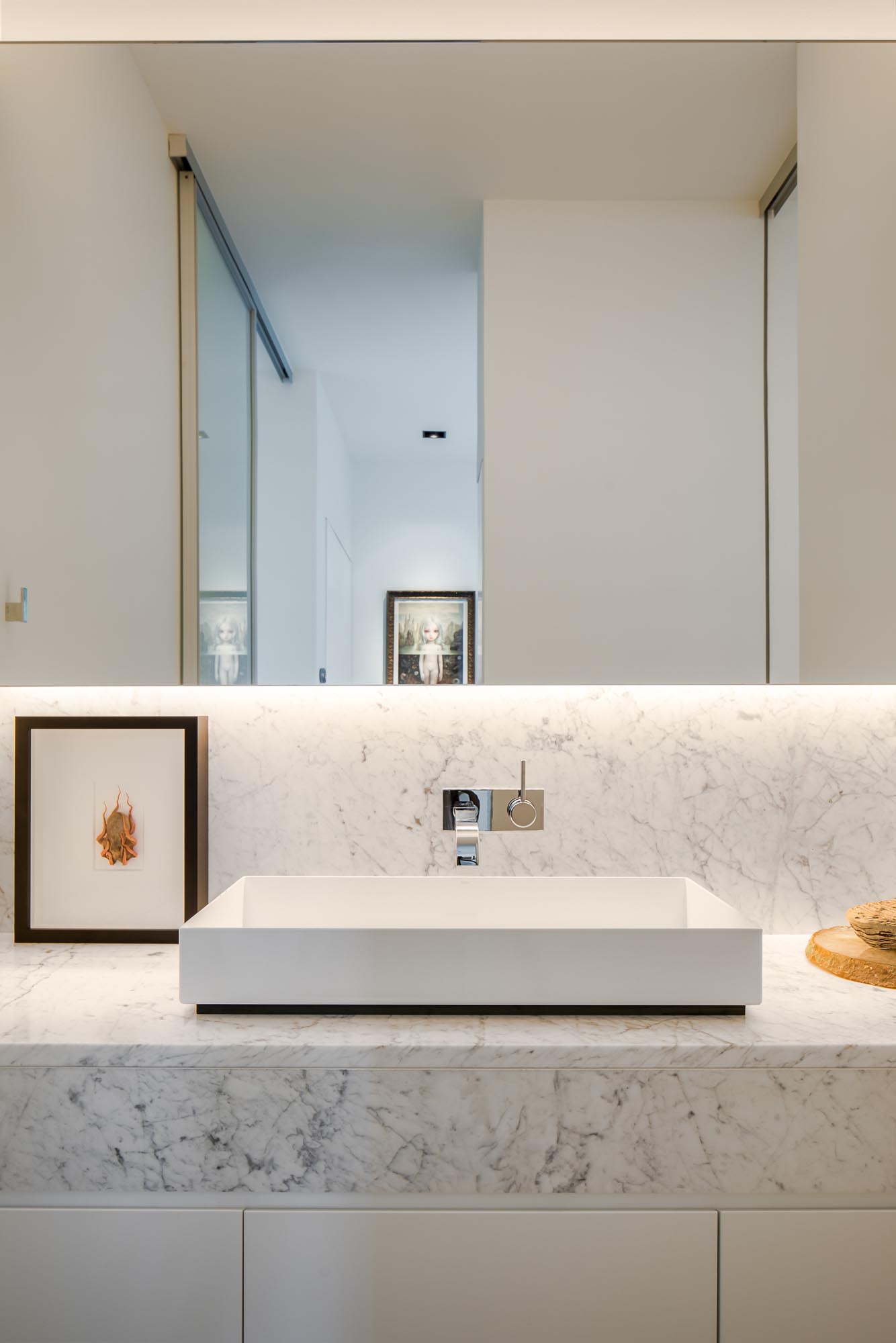 This modern en-suite bathroom has a backlit mirror, a floating vanity, and a walk-in shower with a shelving niche.