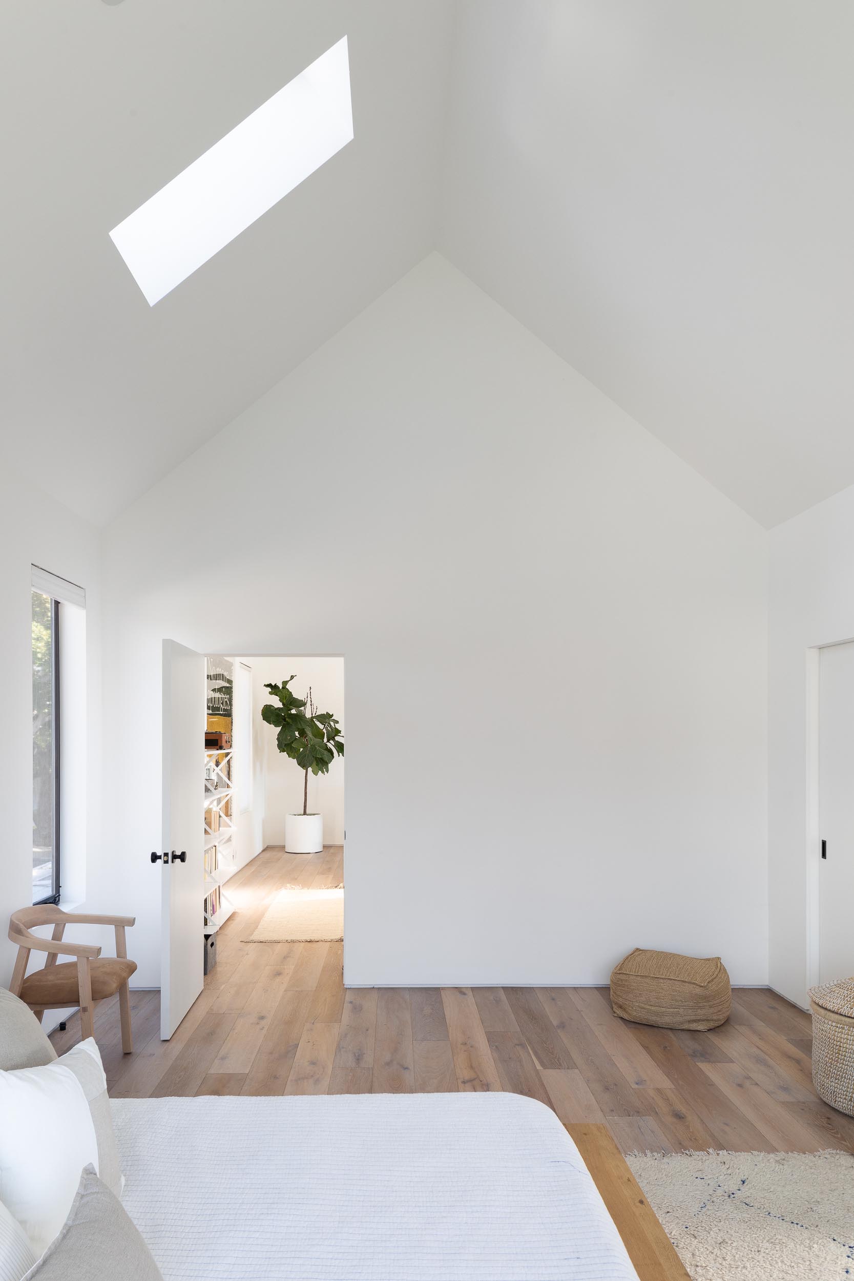 In this modern bedroom, a vaulted ceiling with a skylight makes the room feel large and open, while a wood bed frame and side tables add warmth to the space, and a window seat creates a cozy place to read a book and take in the views of the yard.