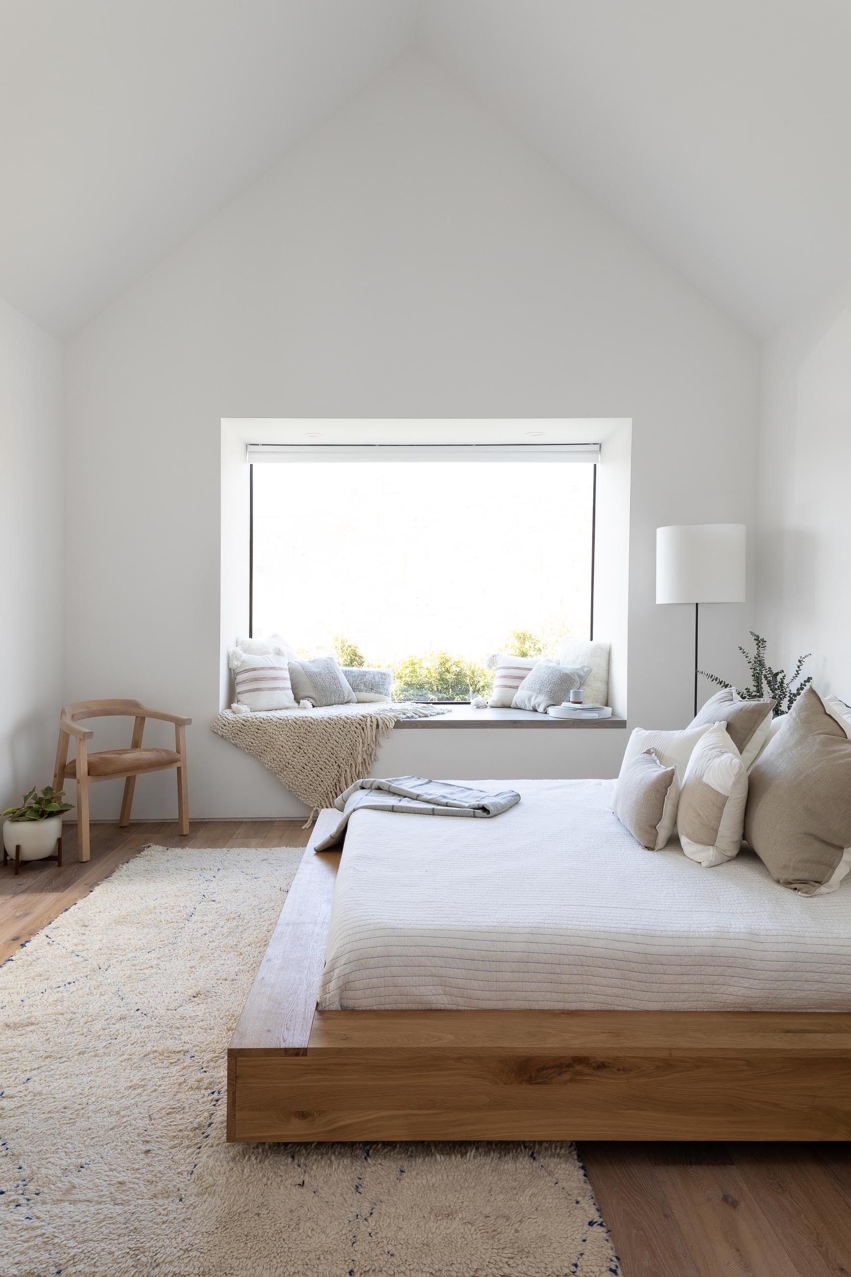 In this modern bedroom, a vaulted ceiling with a skylight makes the room feel large and open, while a wood bed frame and side tables add warmth to the space, and a window seat creates a cozy place to read a book and take in the views of the yard.