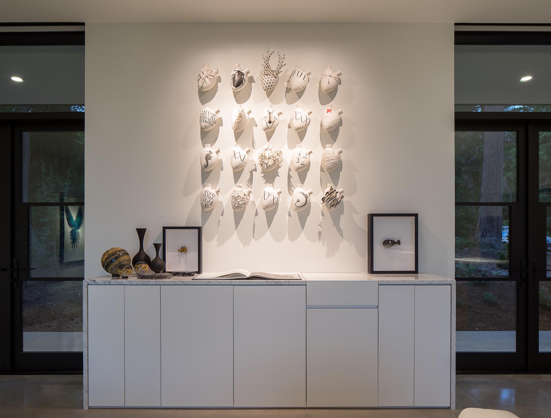 Along the wall in this modern home is a custom-designed cabinet with artifacts, and books, while above, lighting highlights the art.