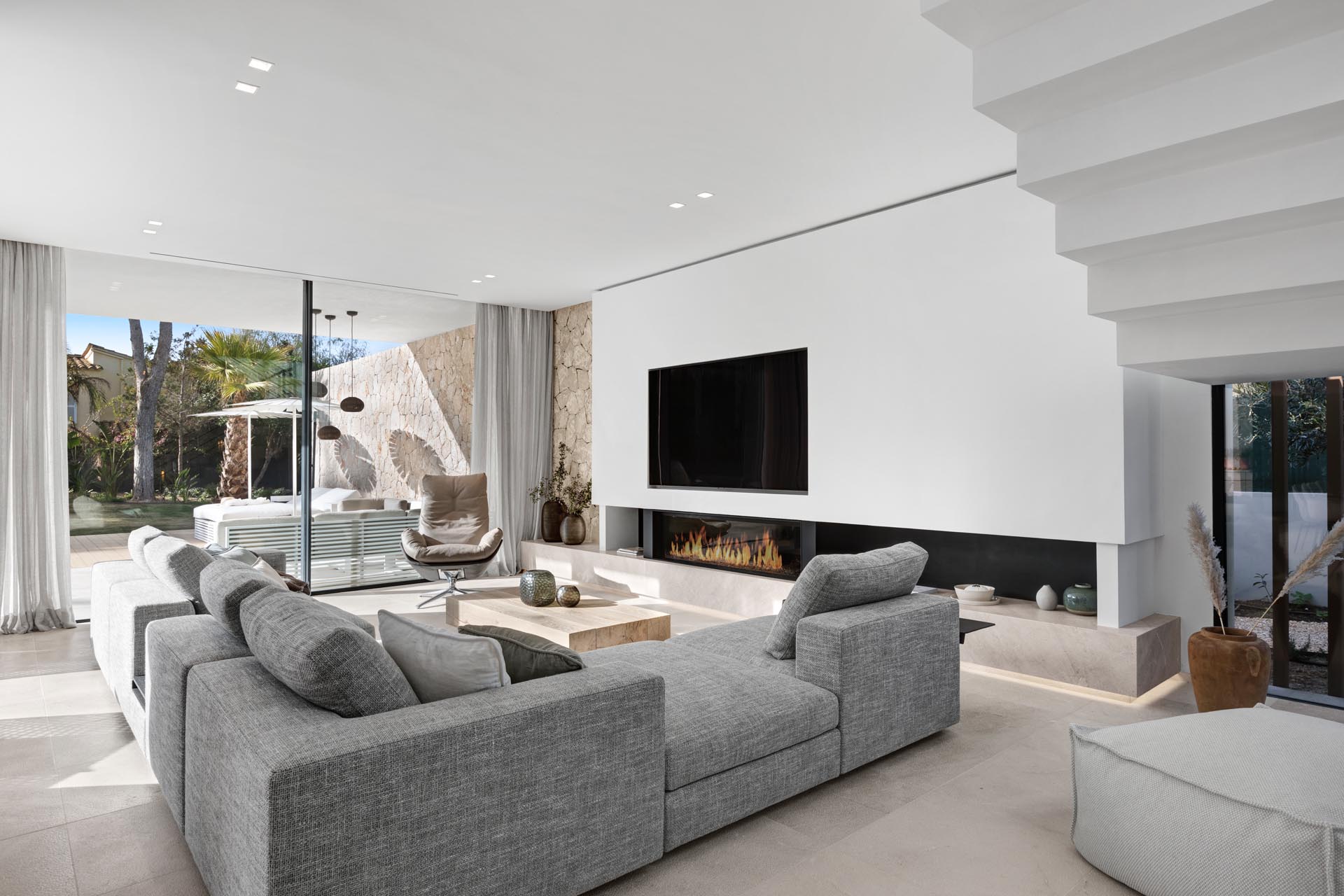 In this modern living room, the L-shaped gray sofa is focused on the linear fireplace with the TV above it. Underneath, there's a Balearic gray limestone hearth with hidden lighting that highlights the floor.