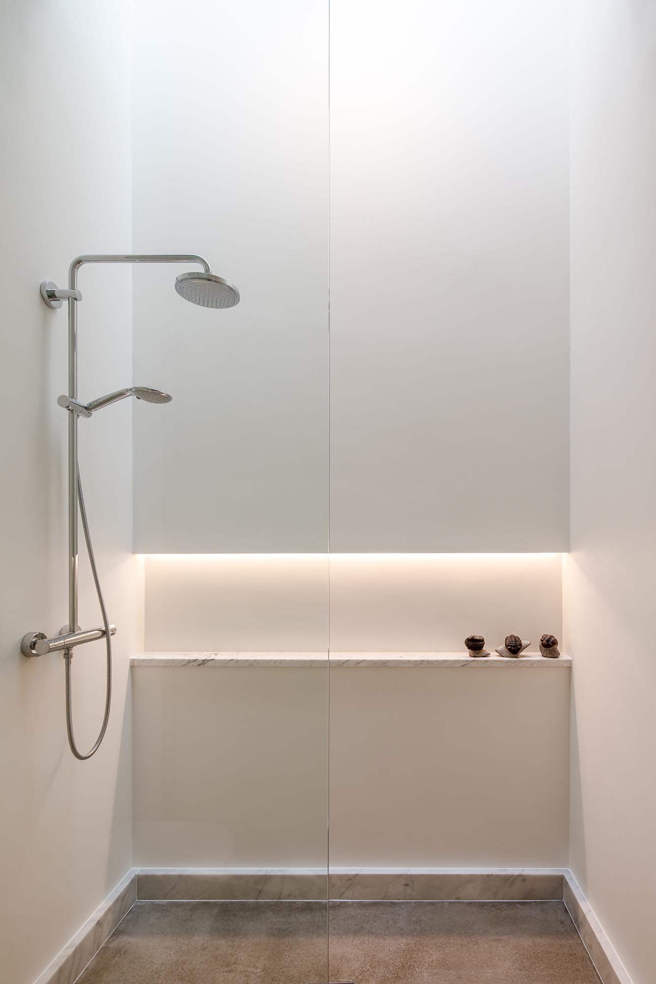 This modern en-suite bathroom has a backlit mirror, a floating vanity, and a walk-in shower with a shelving niche.
