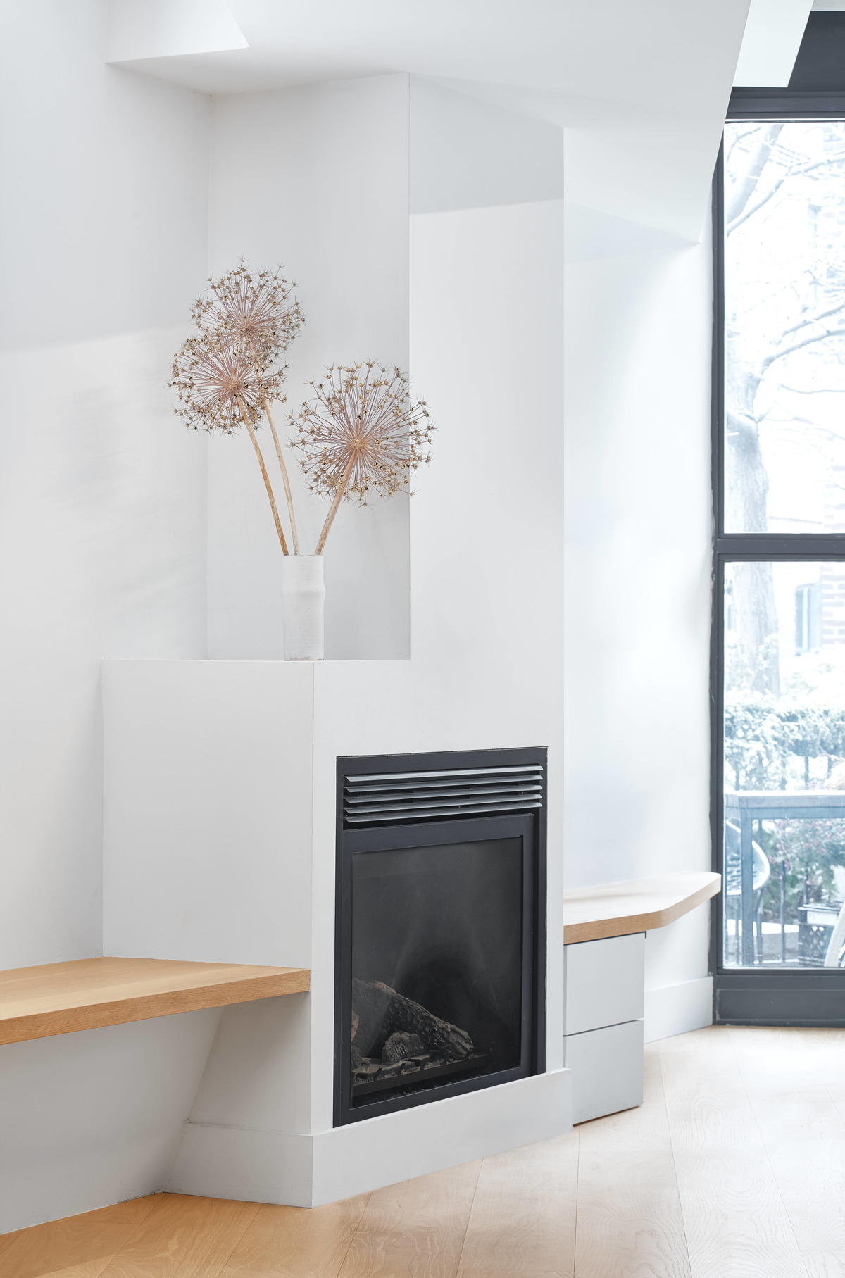 A matte black fireplace surrounded by white walls, oak wood shelving, and wood floors.