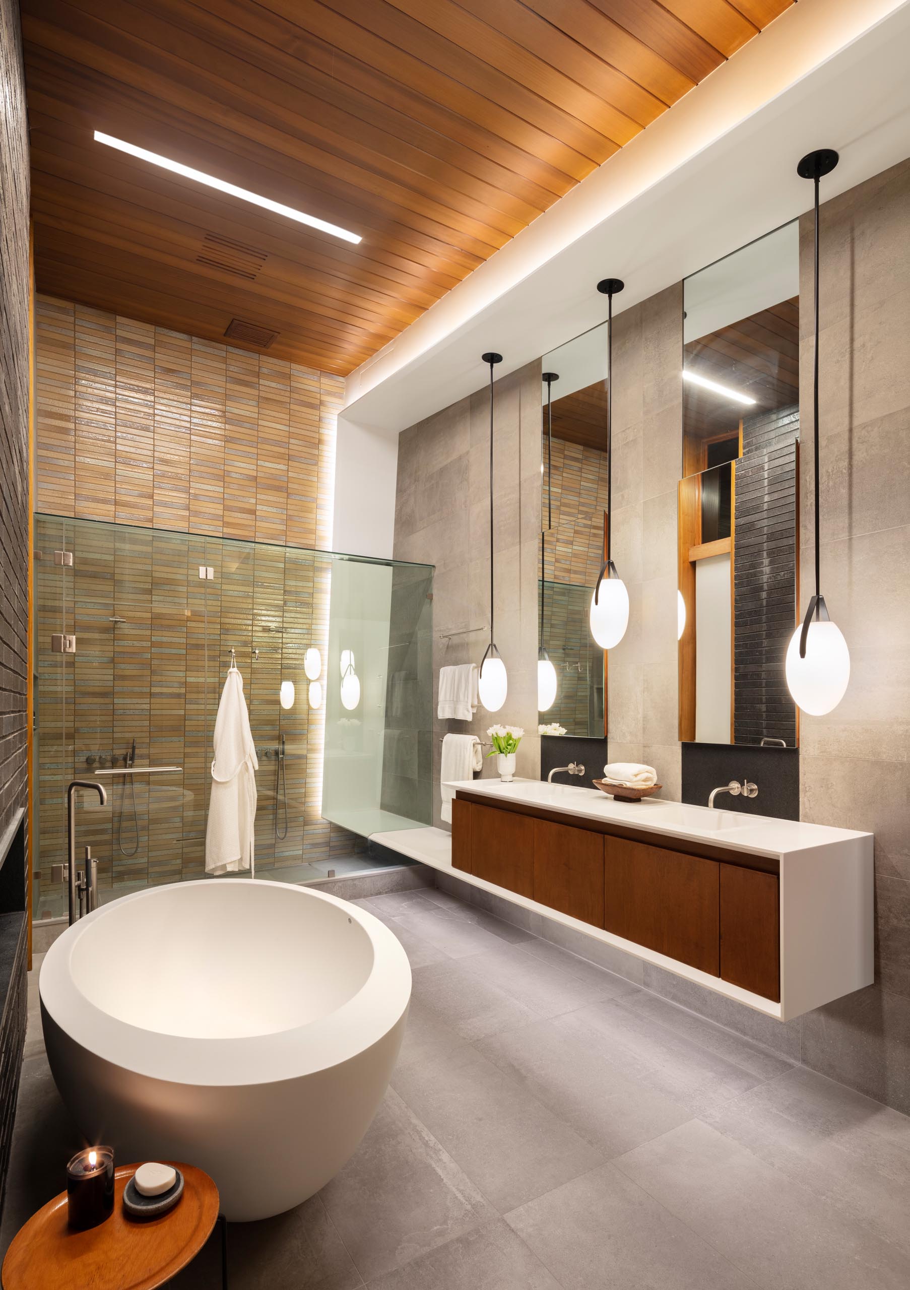 In this modern bathroom there's high ceilings, a freestanding bathtub, and a vanity with three pendant lights hanging above it.