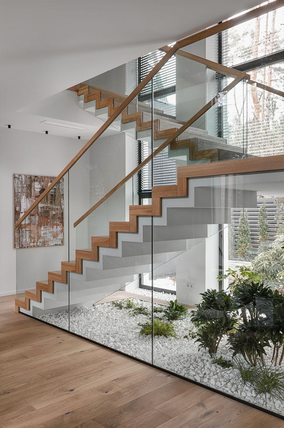 Những cầu thang hiện đại kết nối các tầng khác nhau của ngôi nhà được làm bằng bê tông, gỗ và kính.  Bên dưới cầu thang, đá và cây sống trong nhà đã được sử dụng để tạo ra một khu vườn nhỏ, mang không gian ngoài trời vào.