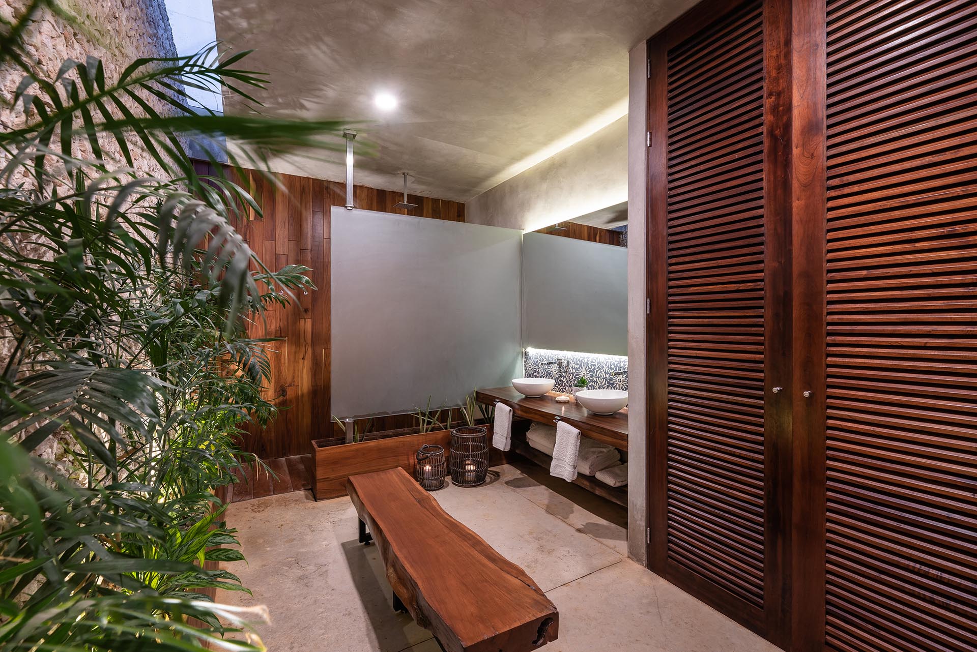 A modern bathroom with wood accents, a backlit mirror, plants, and a skylight.