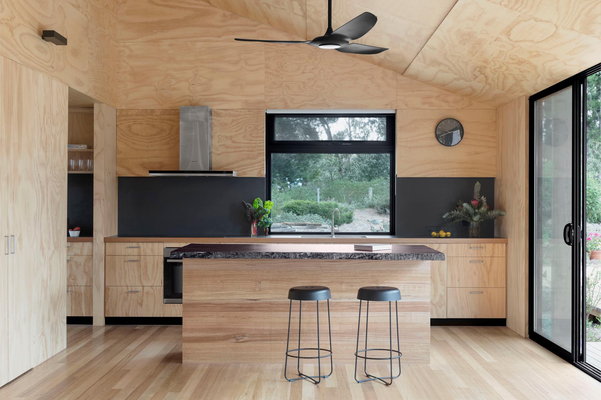 A modern plywood kitchen with a matte black countertop and backsplash.