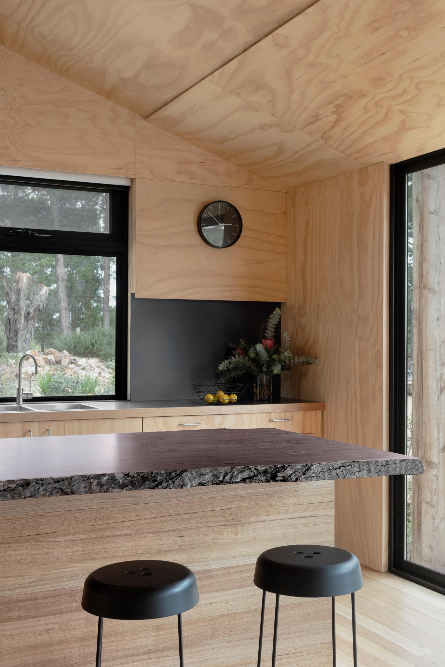 A modern plywood kitchen with a matte black countertop and backsplash, and an island with a live edge wood countertop.