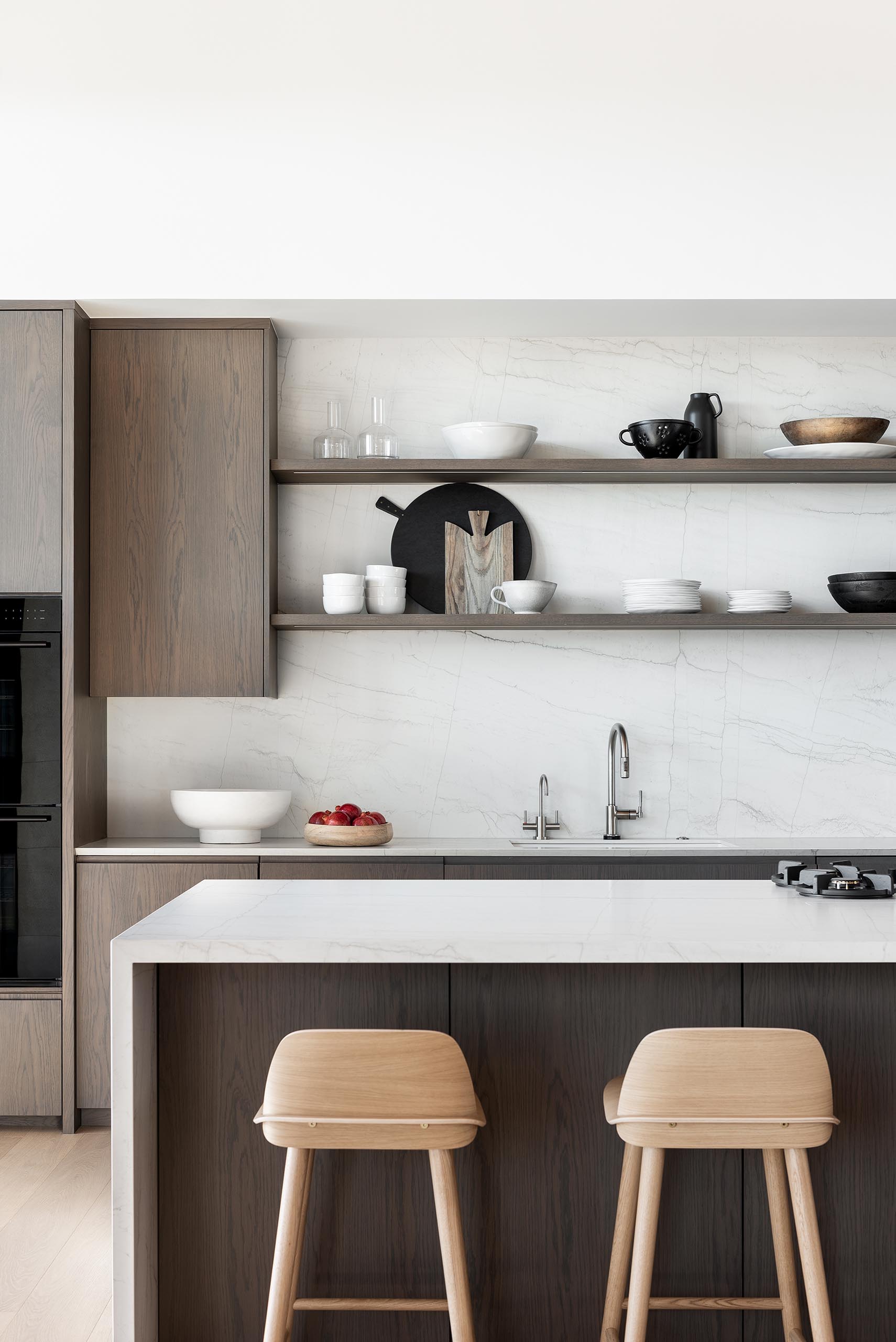 A modern kitchen with wood cabinets, open shelving, and light colored countertops.