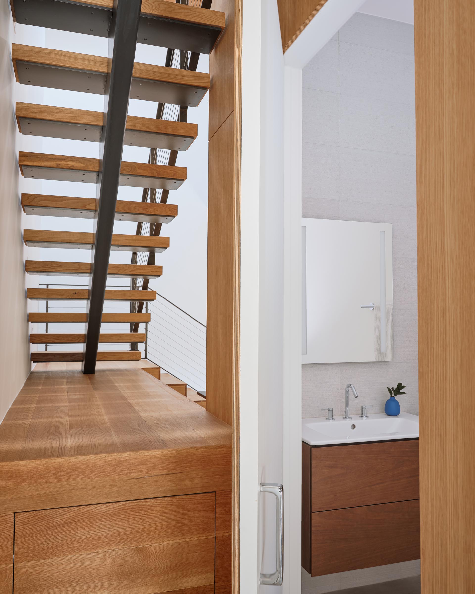 A modern powder room with a wood vanity that matches the door and the wood featured on the stairs.