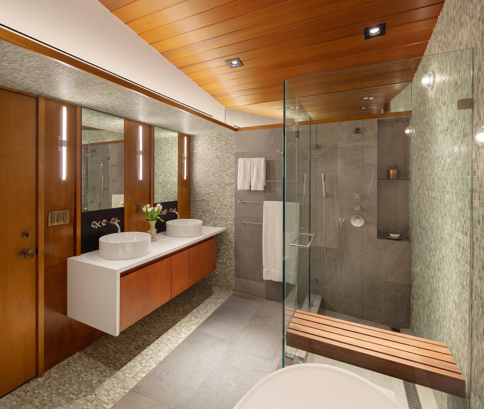 In this modern bathroom, there's a wood ceiling that complements the vanity, while a frameless shower screen provides separation from the bathtub.