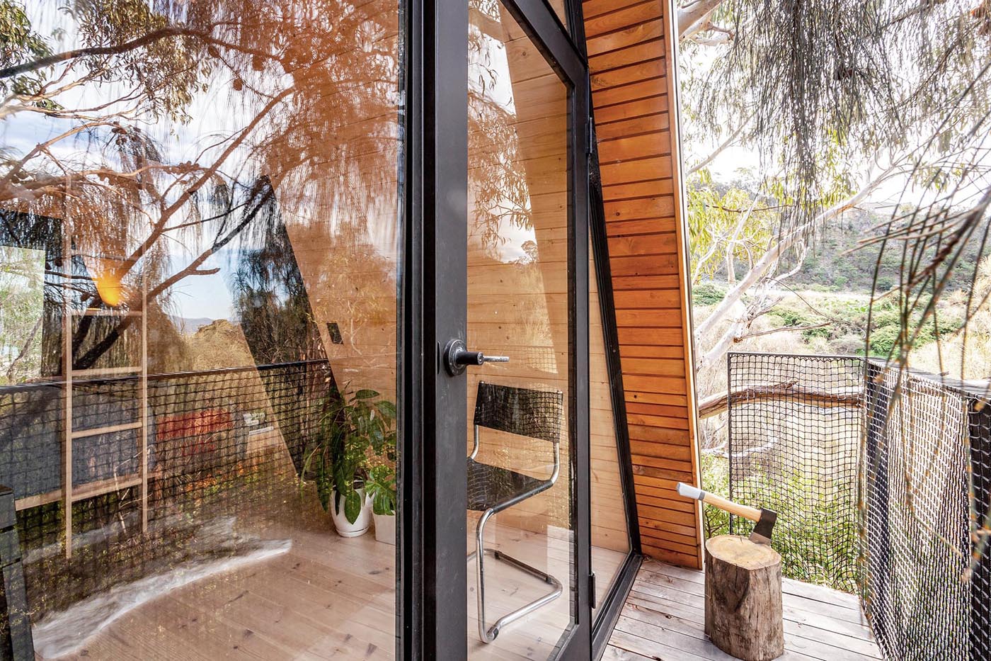 A small and modern wood-lined A-framed cabin with walls of windows at each end.