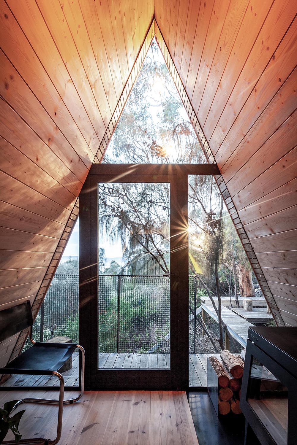 A small and modern wood-lined A-framed cabin with walls of windows at each end.