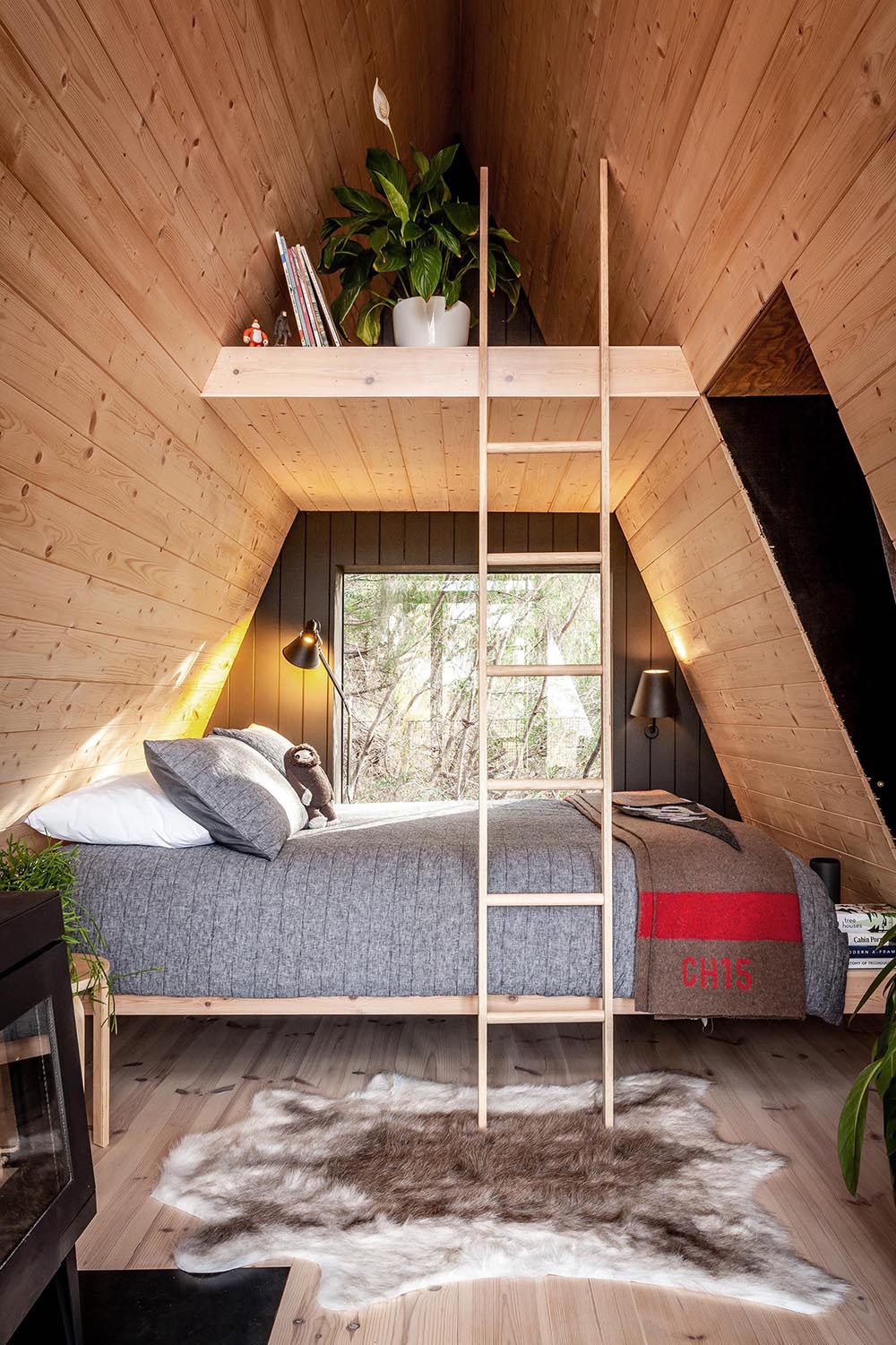 A small and modern wood-lined A-framed cabin with a sleeping area and lofted space.
