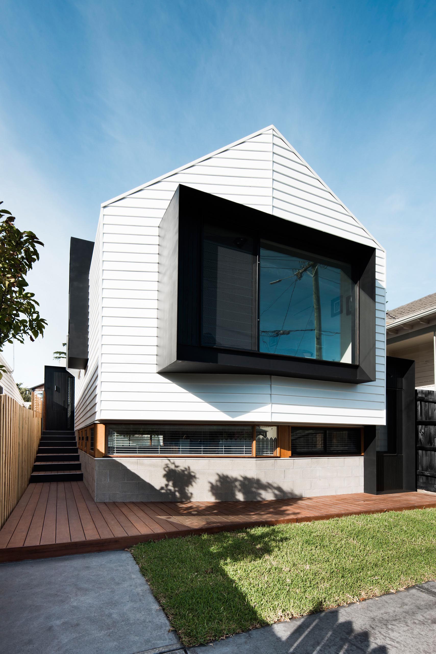 The front of the home has a white exterior which matches the white picket fence, while a large black-framed window protrudes away from the house.