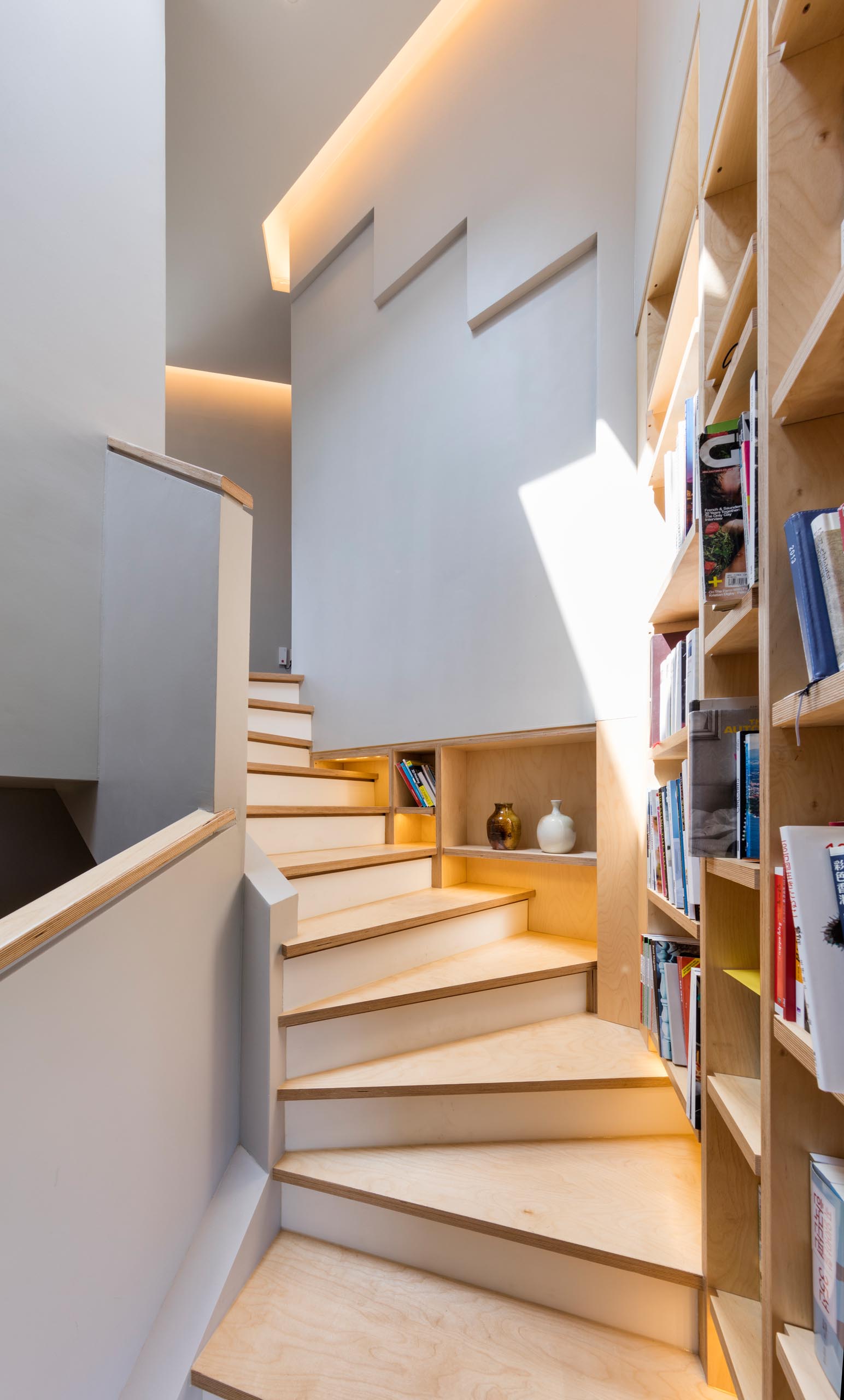 A built-in bookshelf lined with wood that follows the staircase in a modern home.