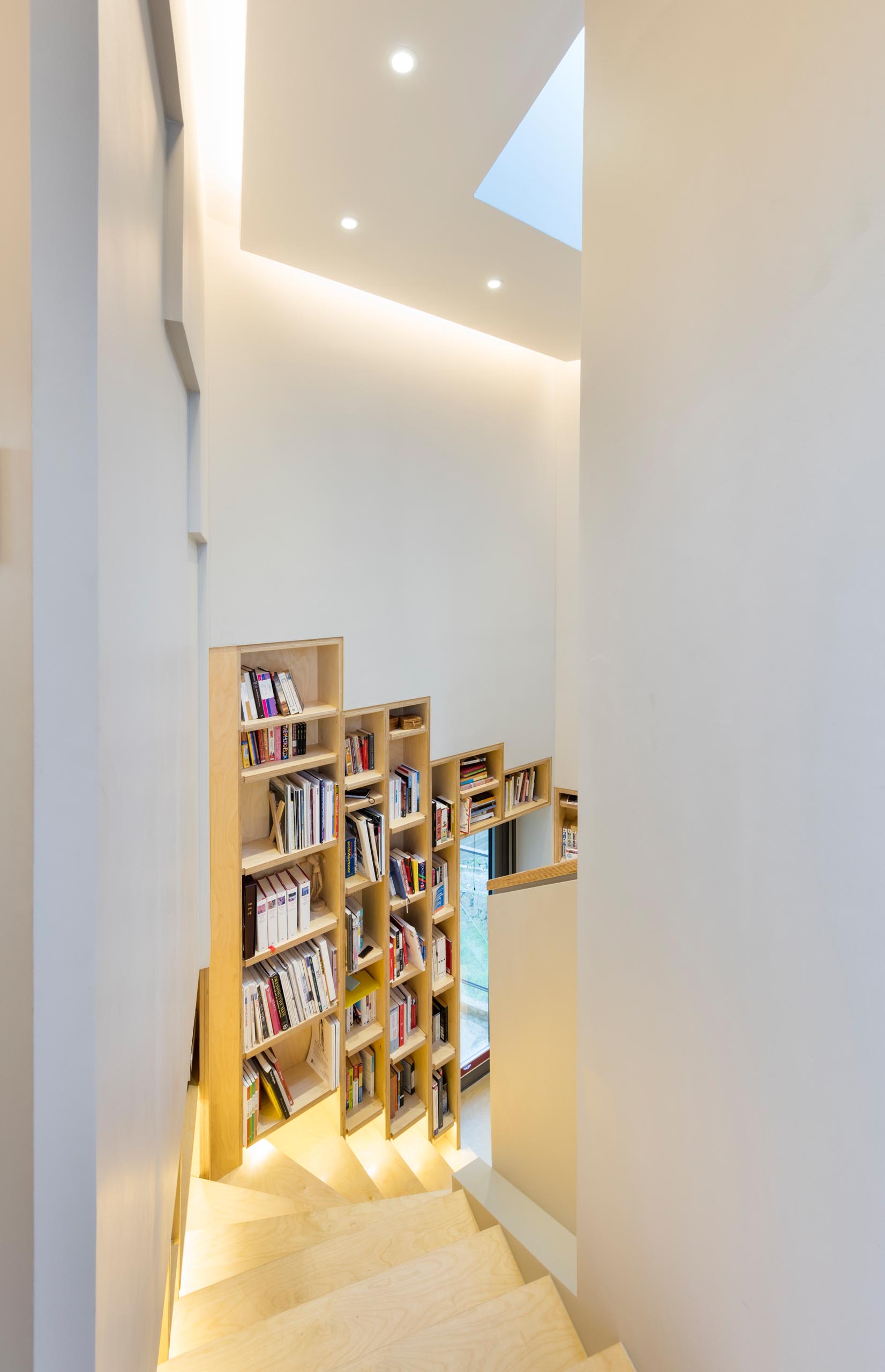 A built-in bookshelf lined with wood that follows the staircase in a modern home.