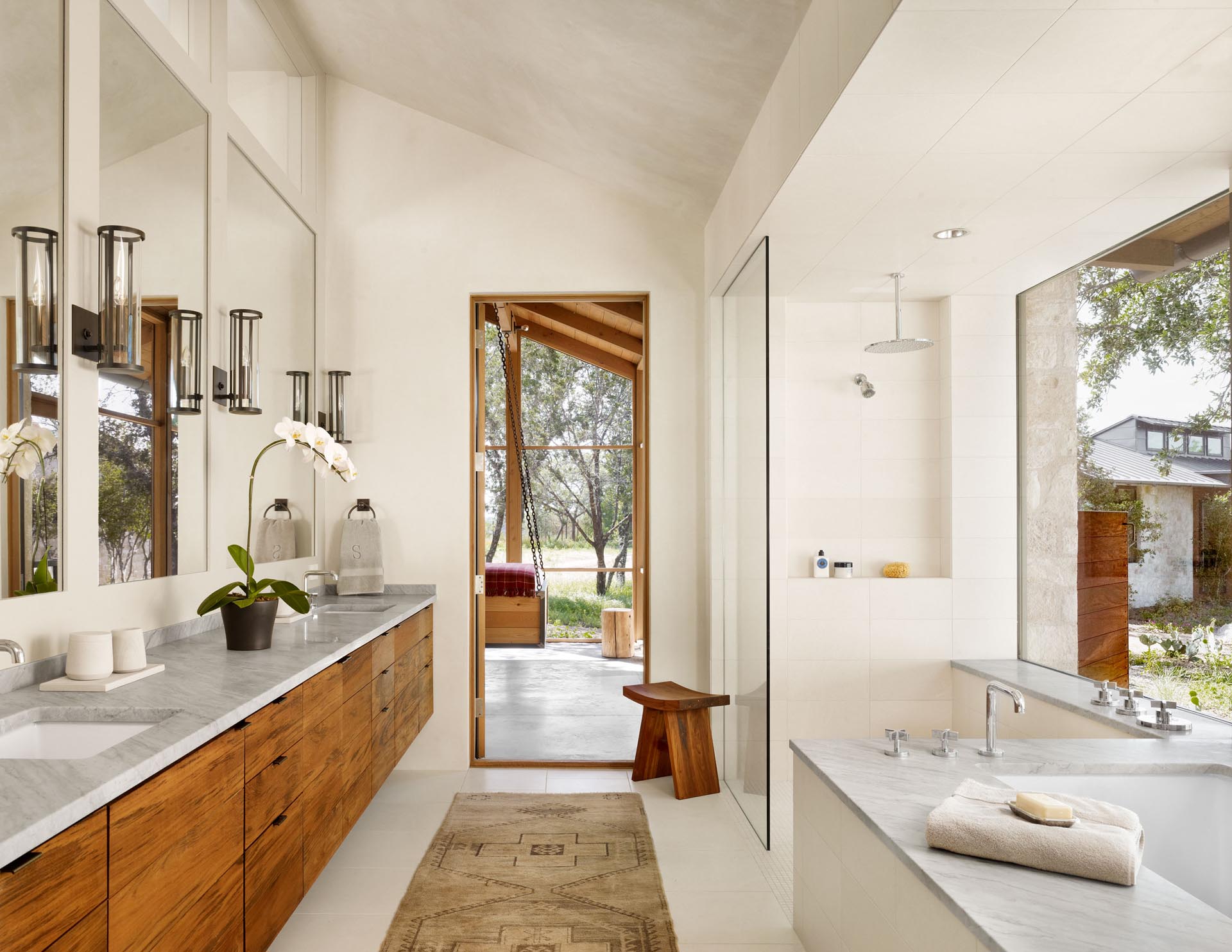 A walk-through bathroom includes a wood vanity that runs the length of the wall, as well as a built-in bathtub and a walk-in shower with an oversized shelving niche.