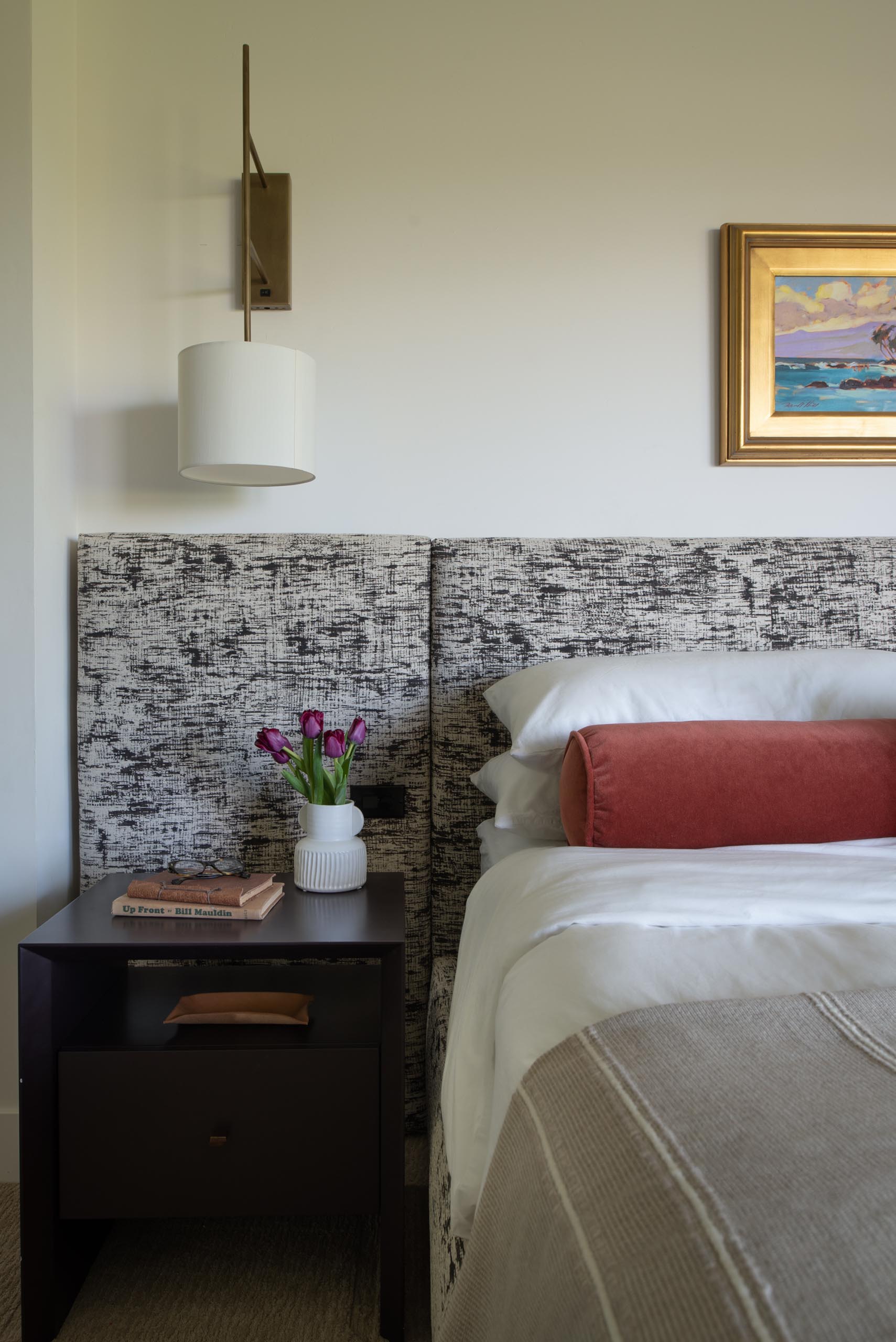 In this primary bedroom, a custom wall to wall headboard in Kelly Wearstler fabric was designed with integrated light switches as well as outlets. The fabric used for the headboard also carries on to the bed frame, while wall lights act as bedside tables.