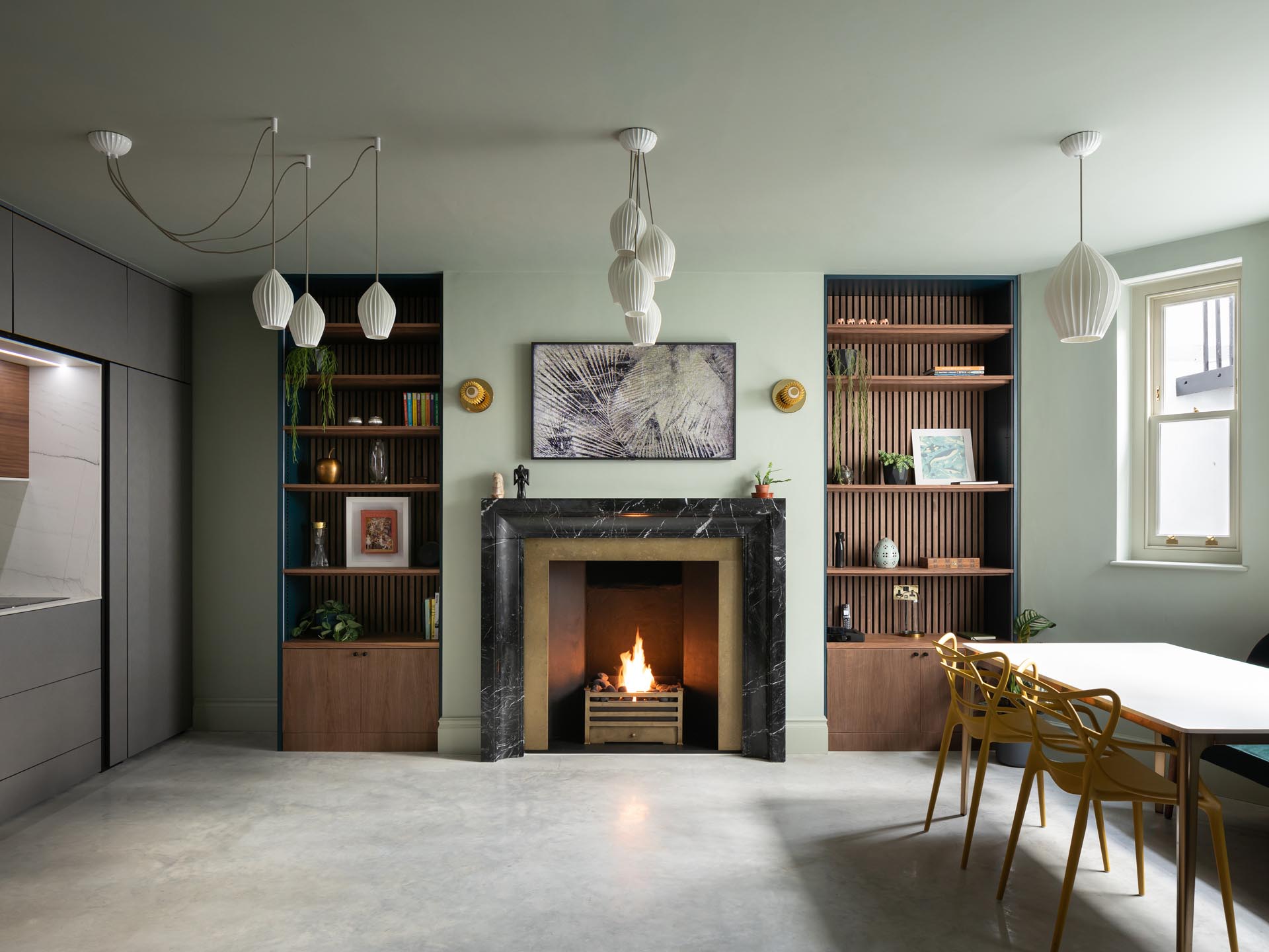 White lighting hangs from the ceiling, while a fireplace is flanked with floor-to-ceiling wood bookshelves.