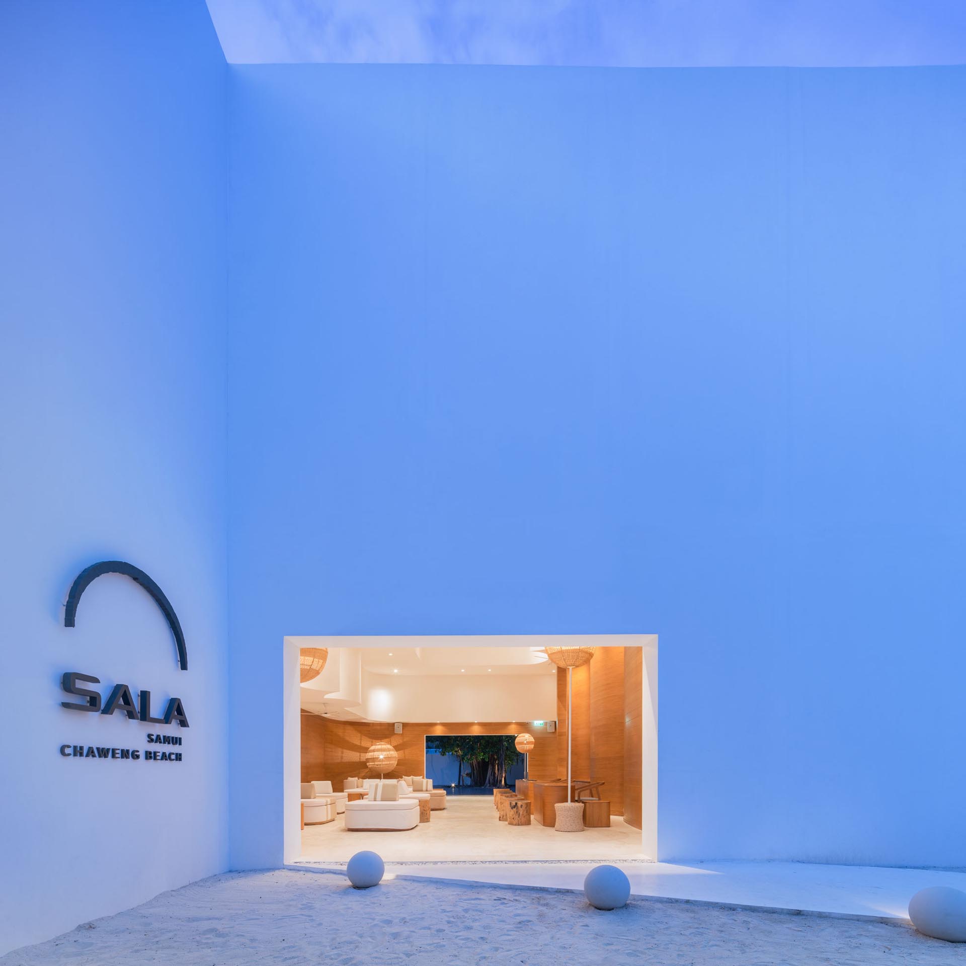 A modern hotel lobby with sculptural wood walls, woven lighting, and round furniture.