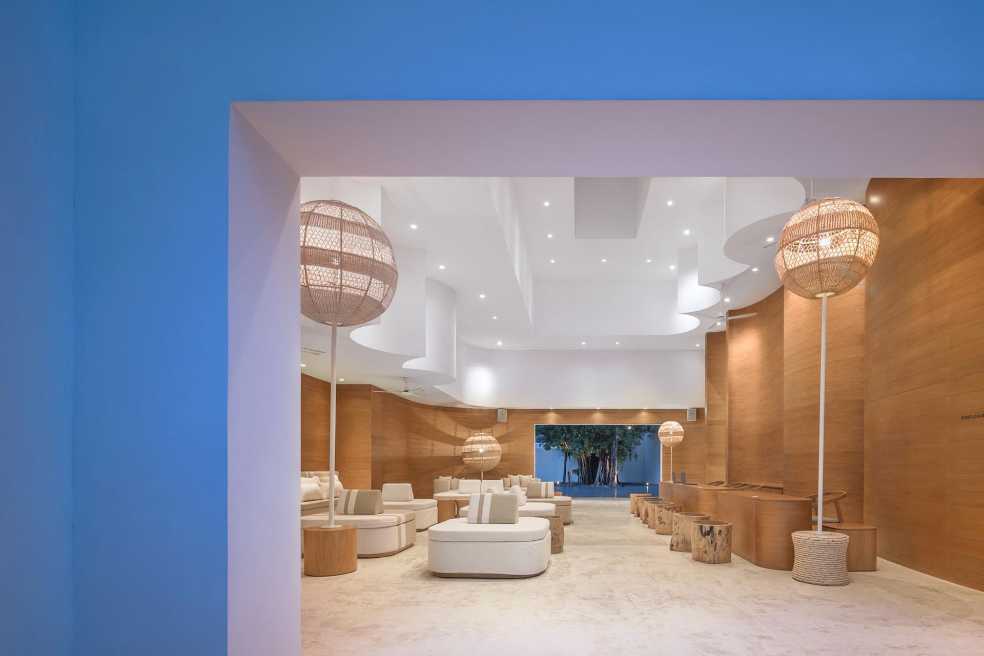 A modern hotel lobby with sculptural wood walls, woven lighting, and round furniture.