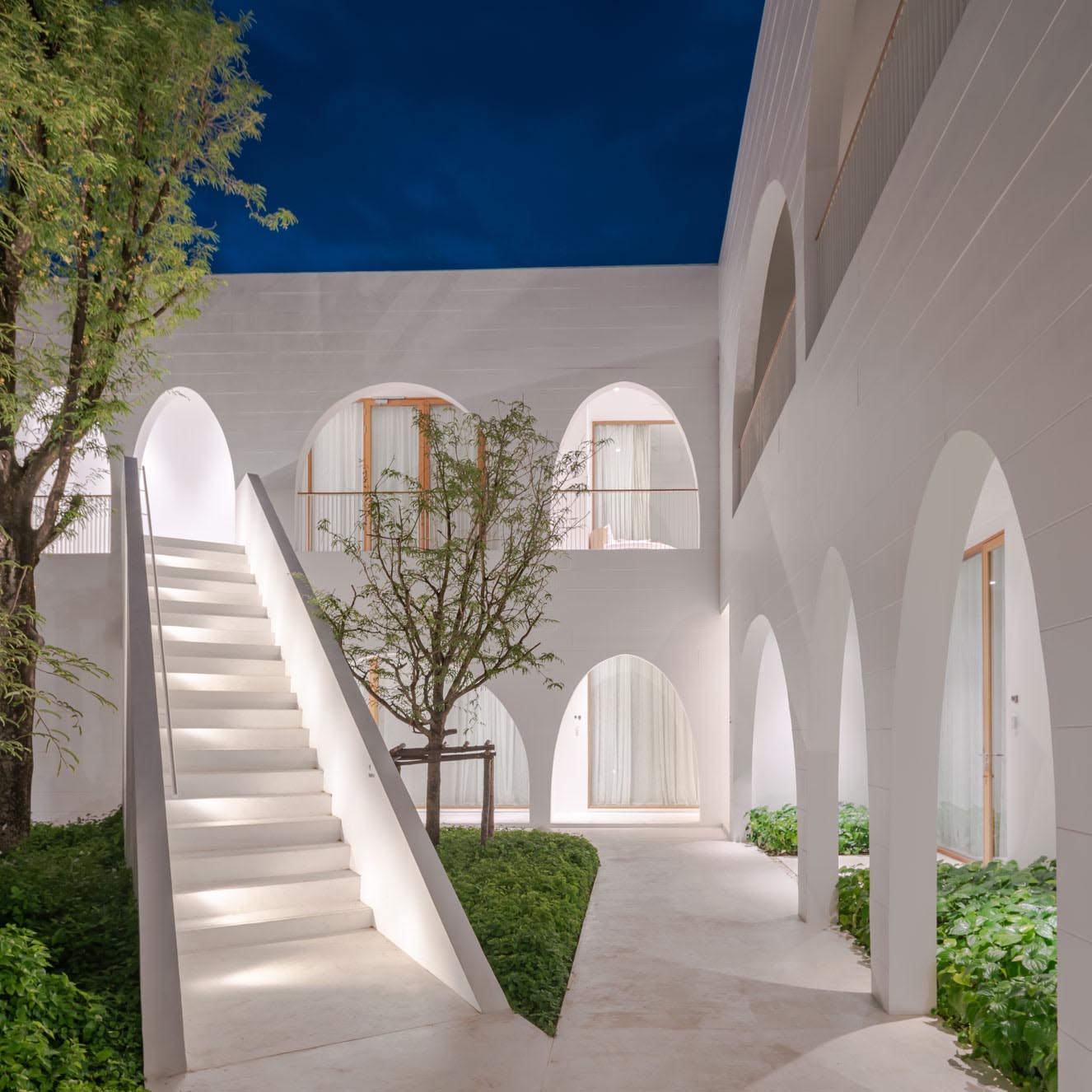 A modern hotel with arches and white stairs with lighting.