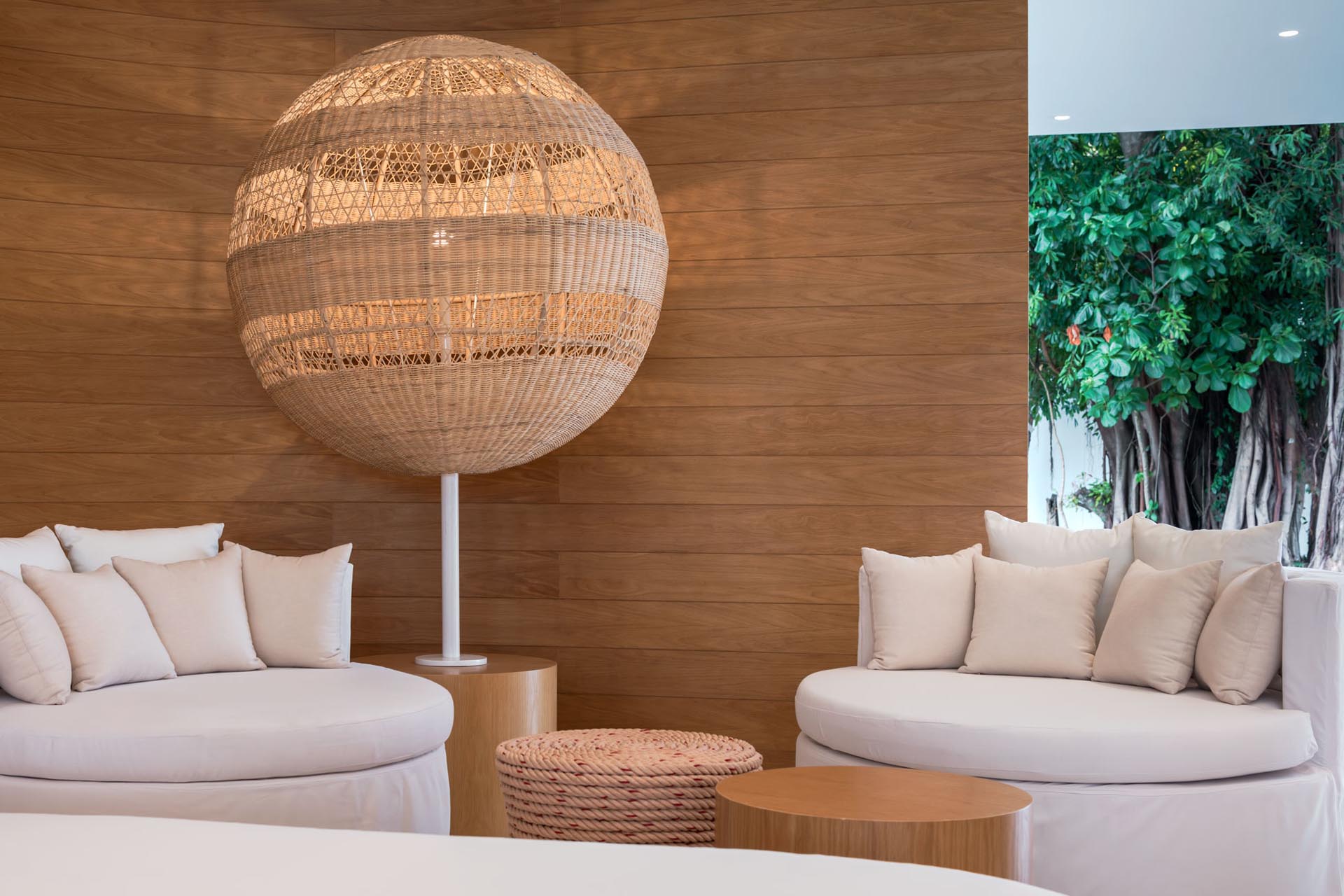 A modern hotel lobby with wood walls, woven lighting, and round furniture.