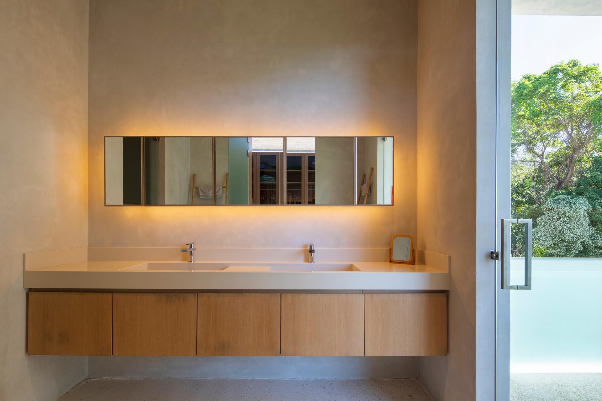 In this modern bathroom a floating wood vanity sits below a horizontal mirror that has a warm glow from the hidden lighting behind it.