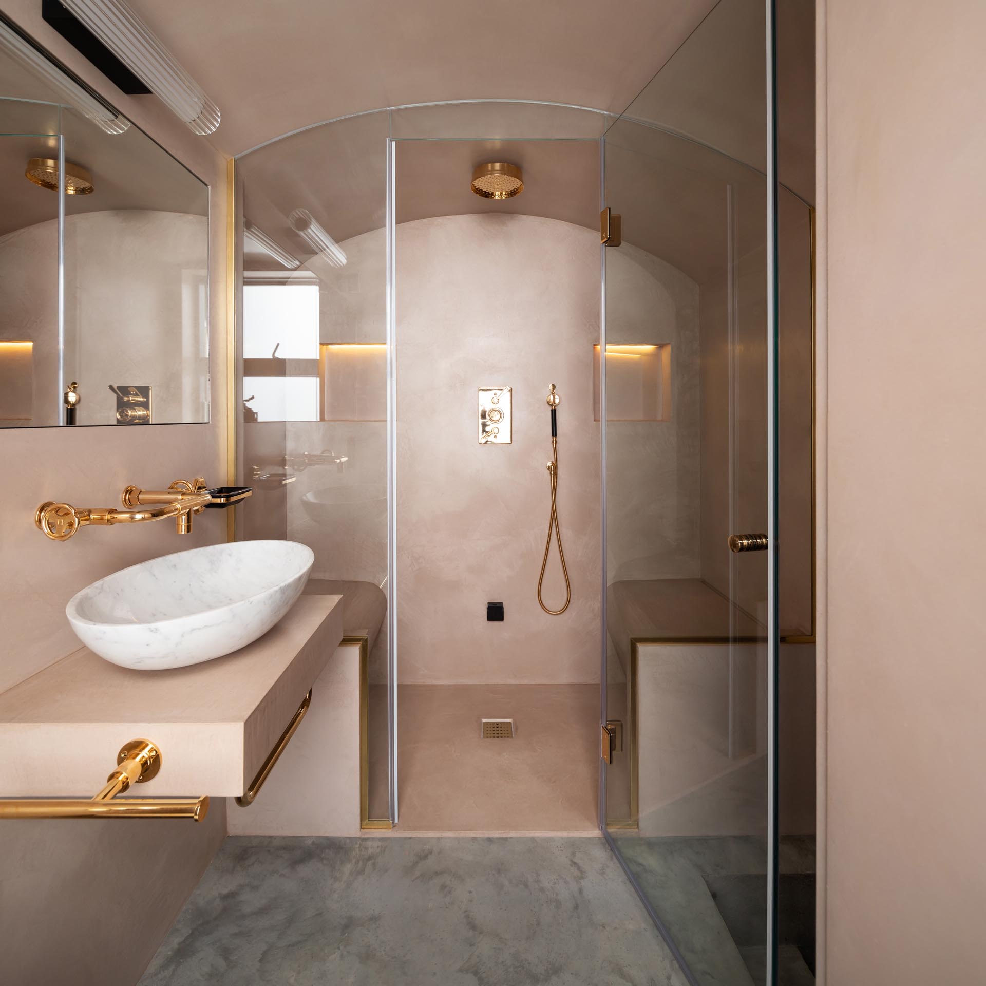 A modern steam room with a curved glass screen, blush pink walls, and rose gold hardware. 