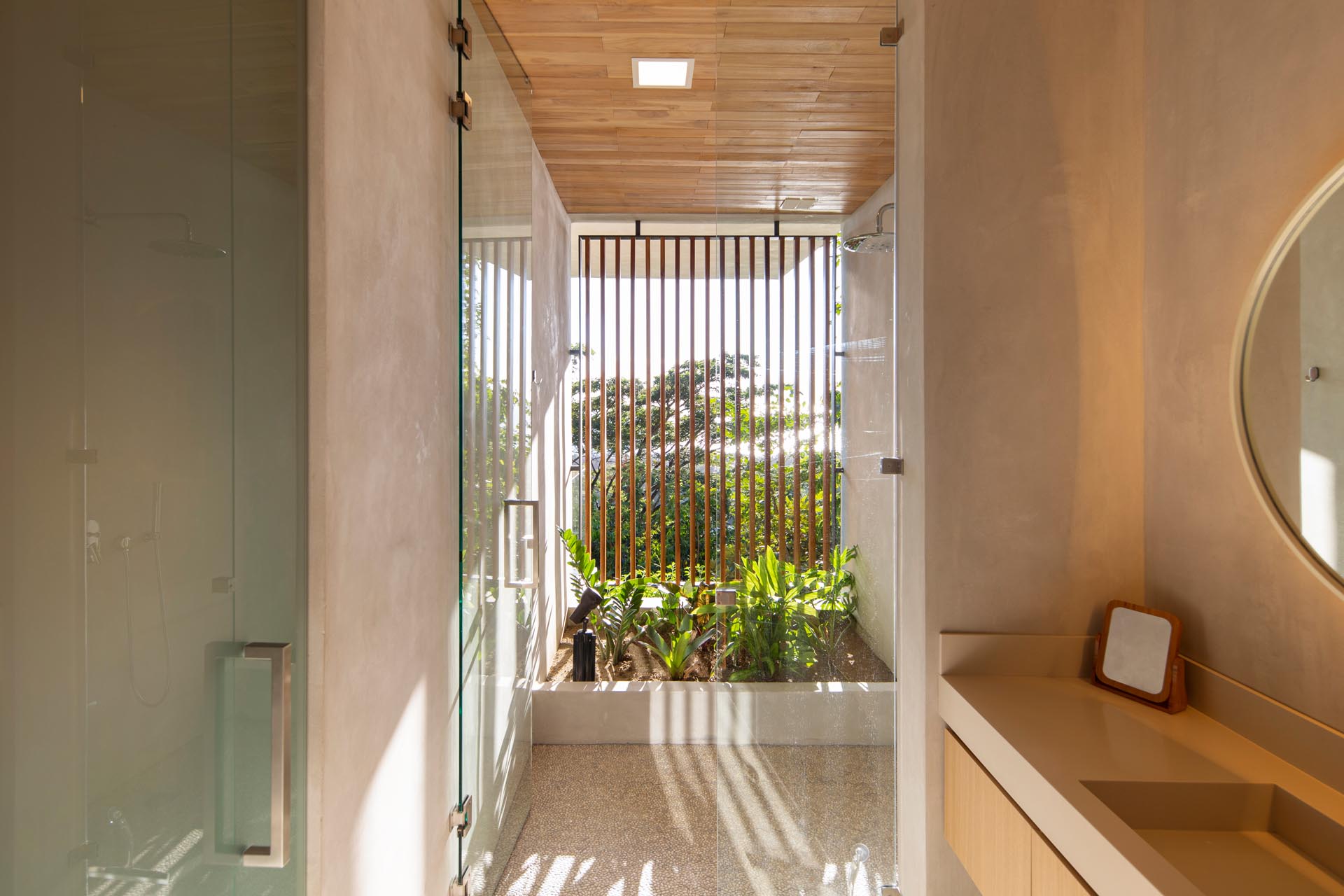 In this modern bathroom, the shower is located in a semi-outdoor room with plants and wood slat screen.