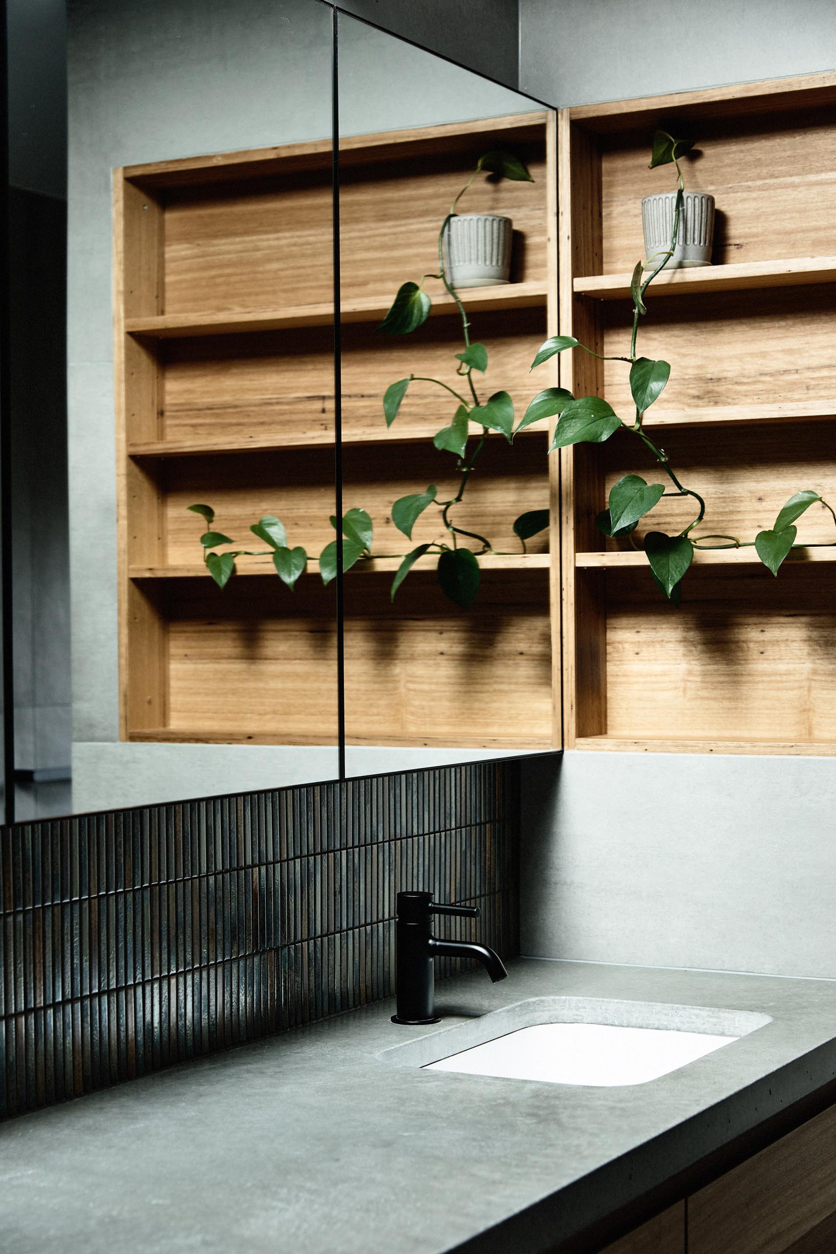 In this modern bathroom, gray walls and floors are accented by a wood-lined shelving niche, small metallic tiles, and a white freestanding bathtub.