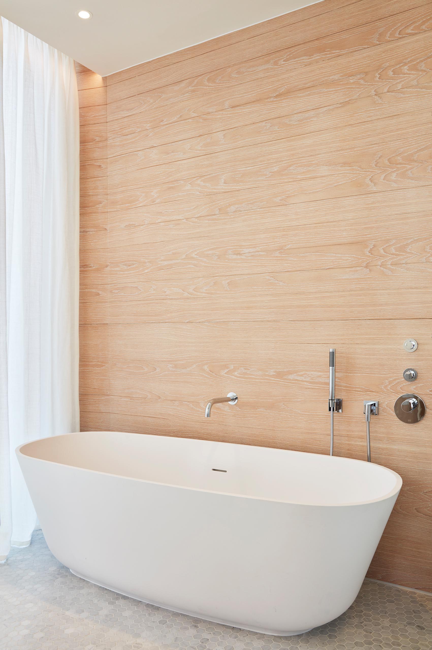 A wood accent wall acts as a backdrop for a freestanding white bathtub.