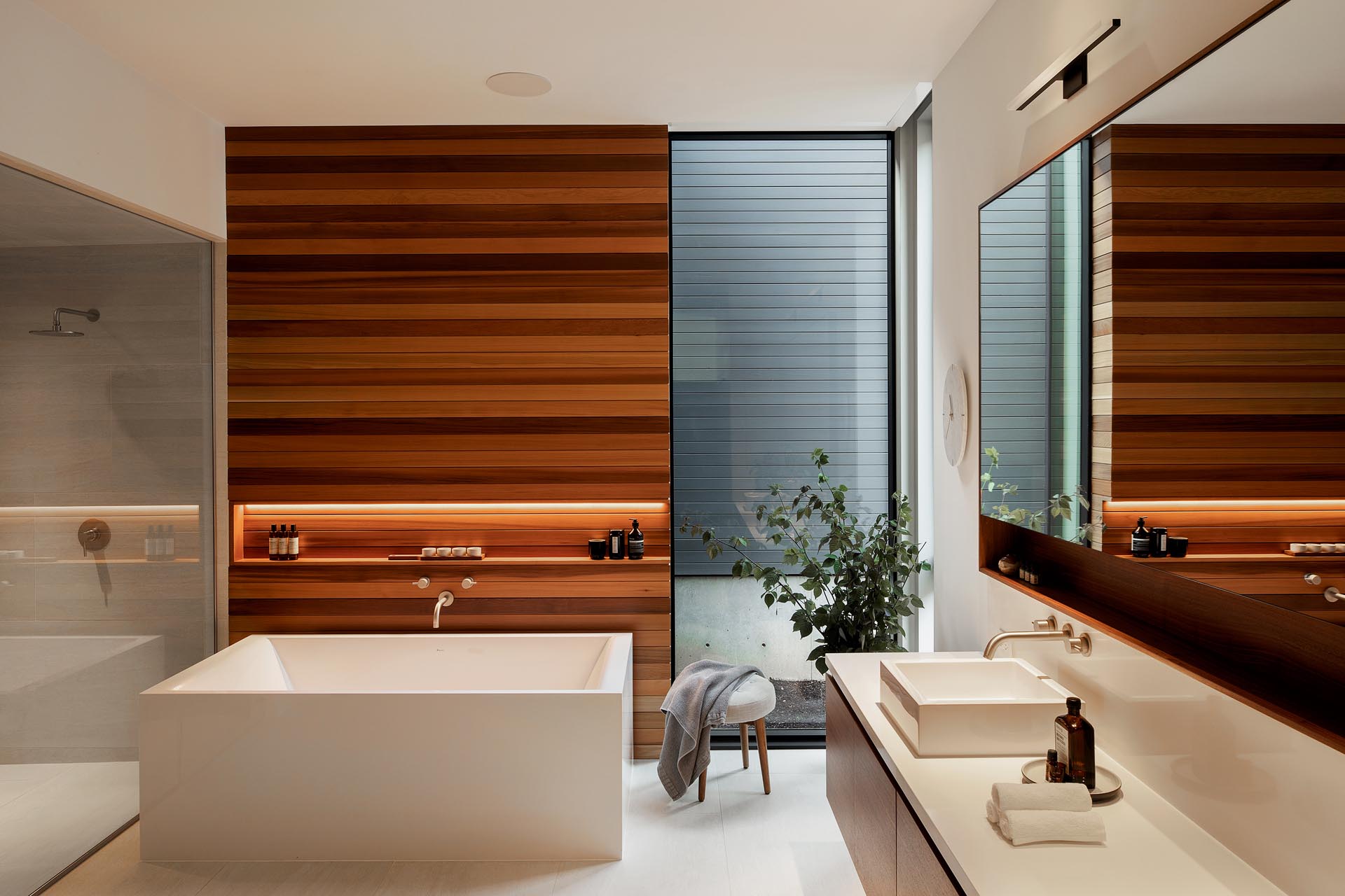 This en-suite bathroom has a warm wood accent wall with varying tones, and includes a horizontal shelving niche with hidden lighting.