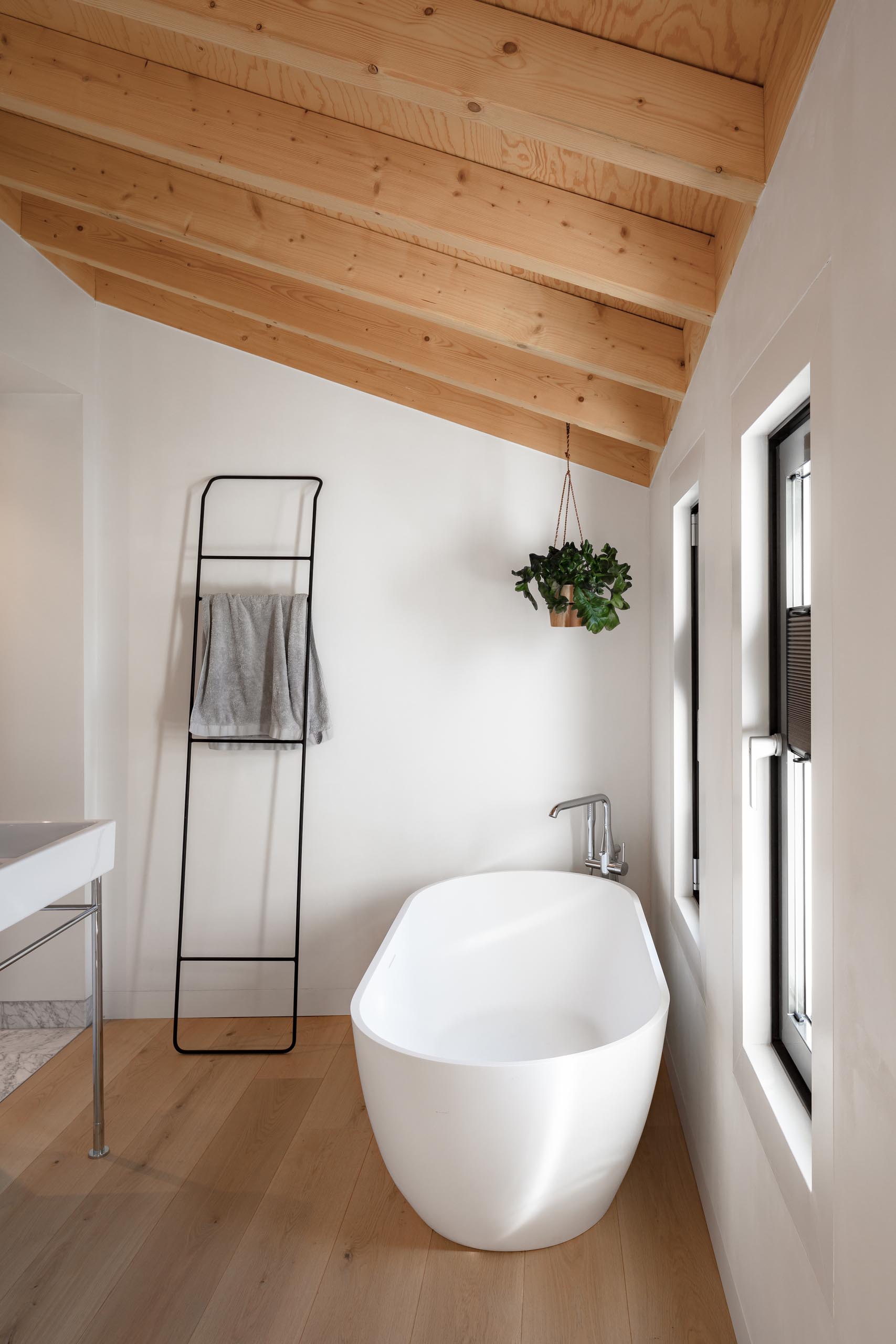 A modern bathroom with an  exposed wood ceiling that complements the wood floor, while the hanging planter in the corner adds a touch of nature.