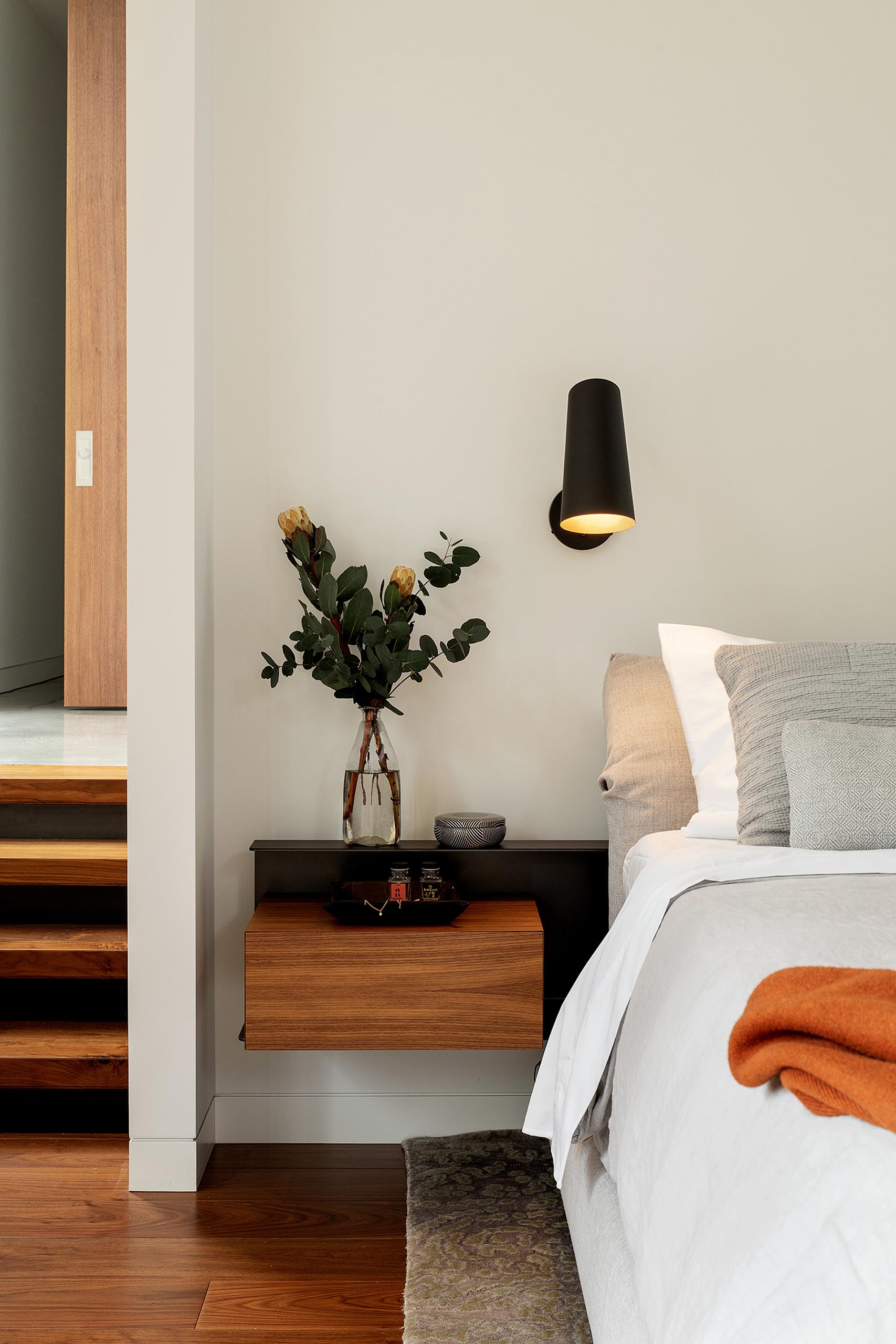 A modern bedroom with a floating bedside table and matte black sconce.
