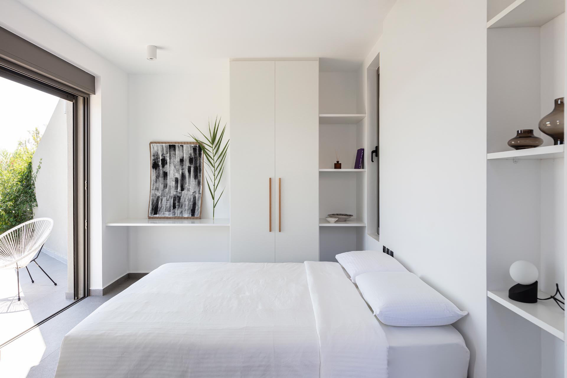 A modern white bedroom with built-in shelves and closets.