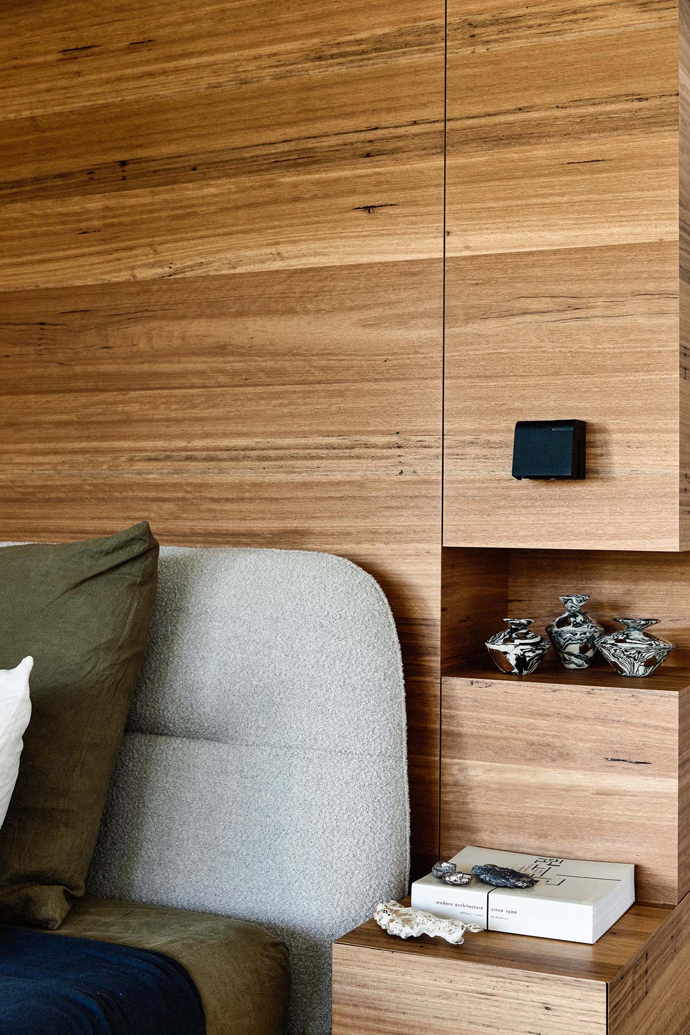 In this modern bedroom, a partial wood wall becomes the backdrop for the bed, and includes bedside tables and shelving niches in its design.