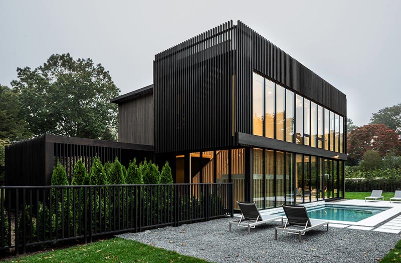 A modern two story black house with walls of windows.