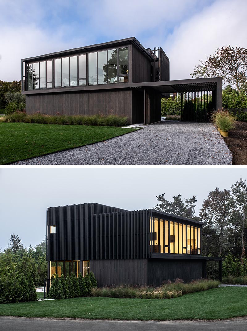 A modern two story black house with walls of windows.