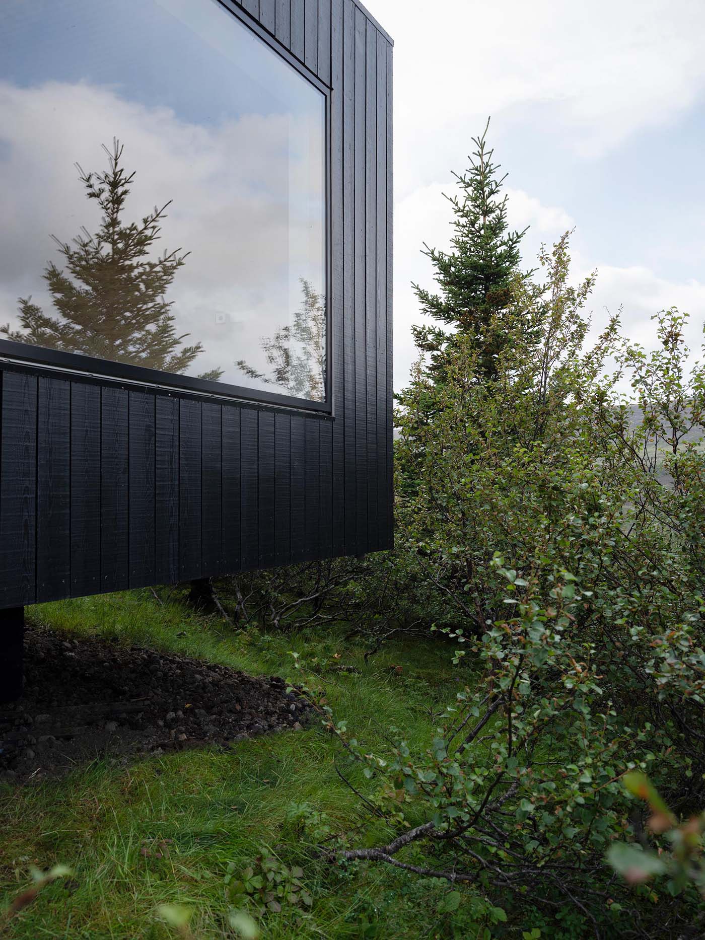 A modern house with blackened wood siding and picture windows.