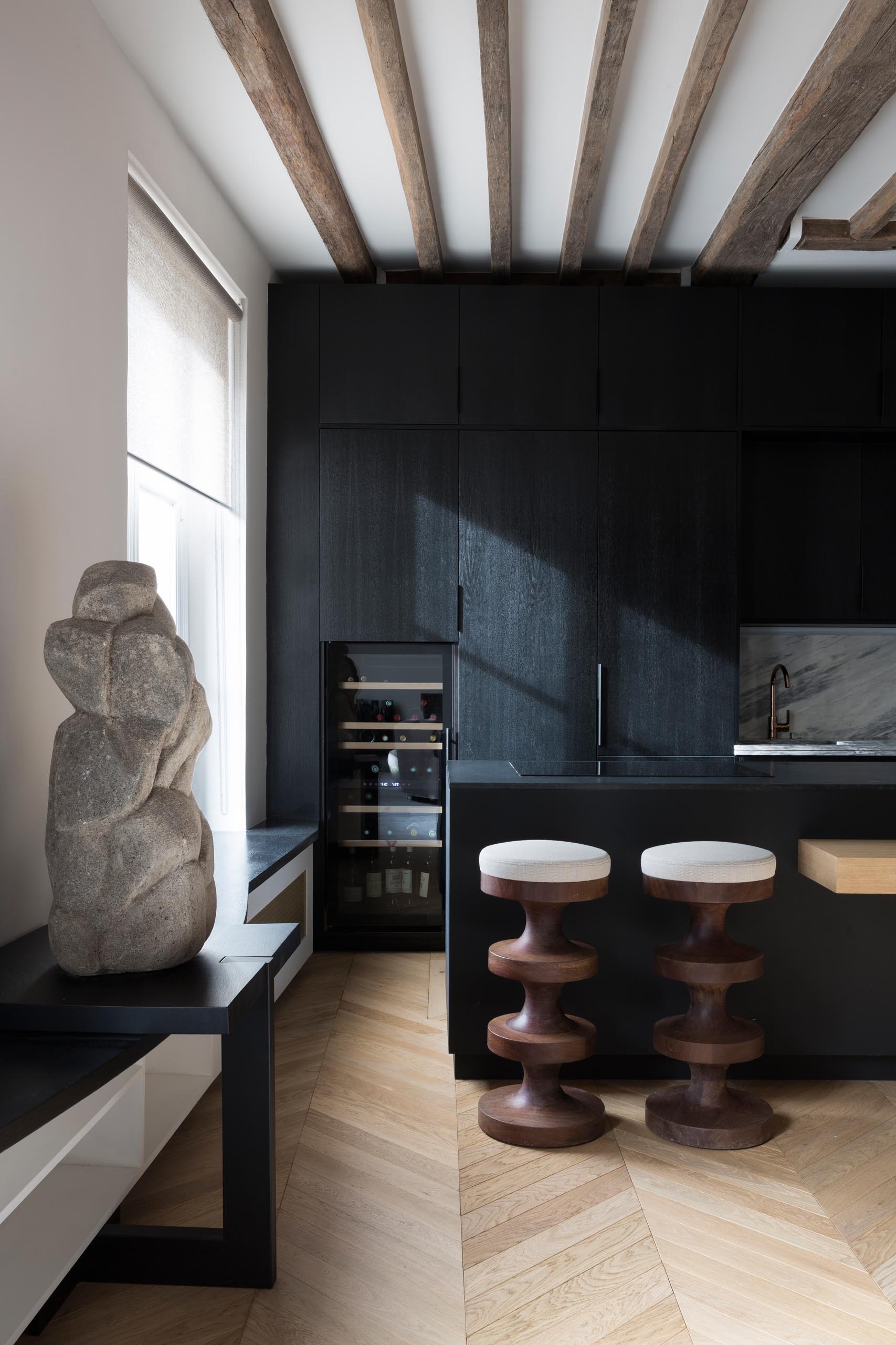 A modern matte black kitchen with a wine fridge and exposed wood beams.