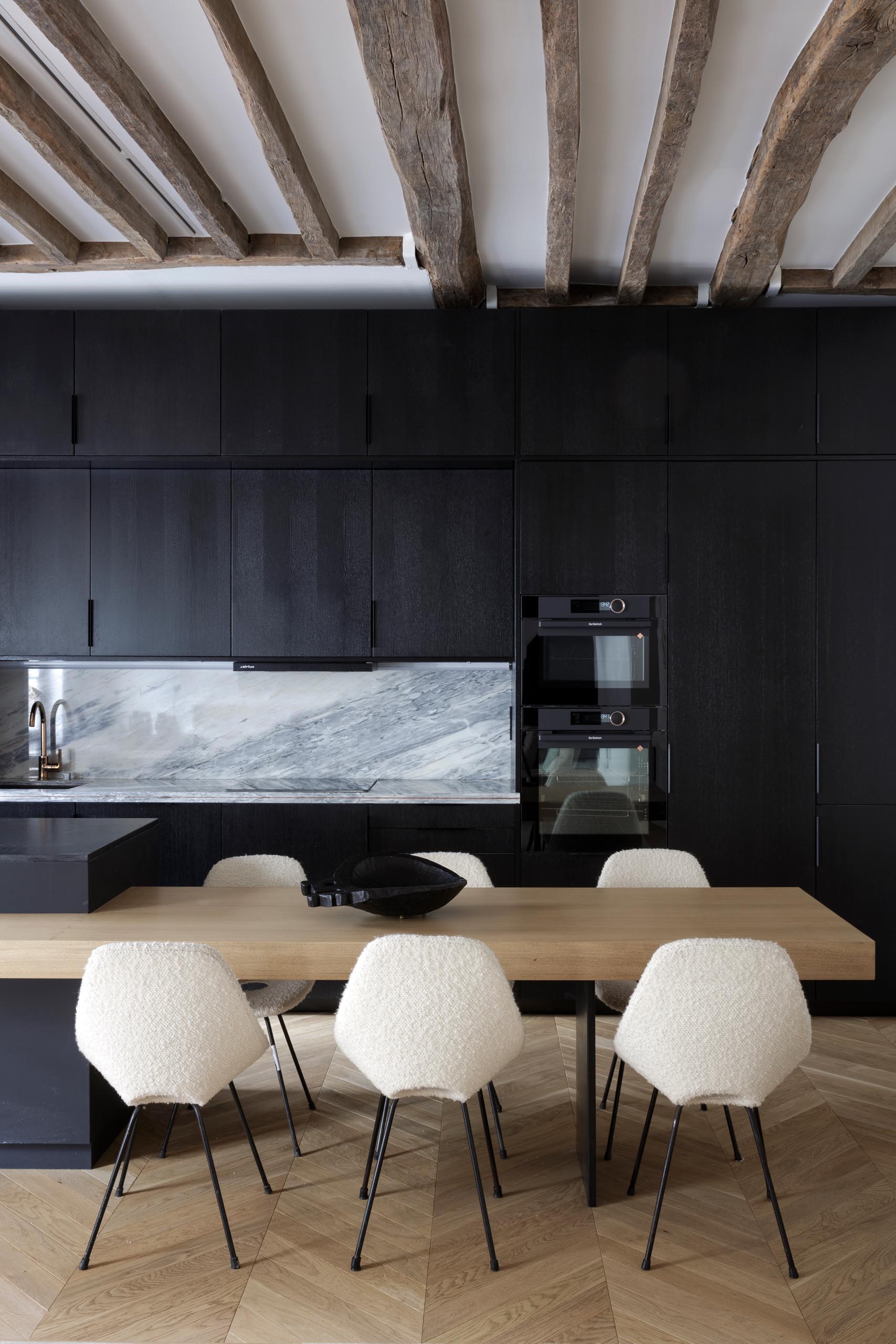 A modern matte black kitchen with a black appliances and exposed wood beams.