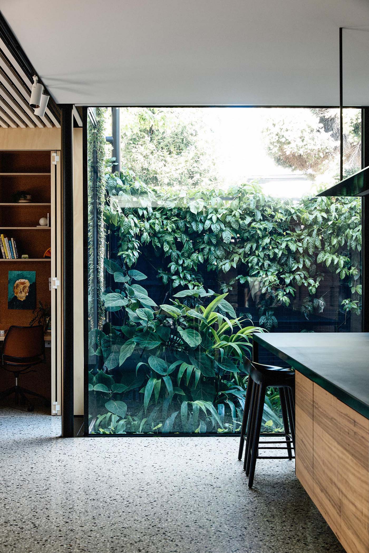 A home office tucked into a closet is adjacent to a large window that provides an unobstructed view of the garden outside.