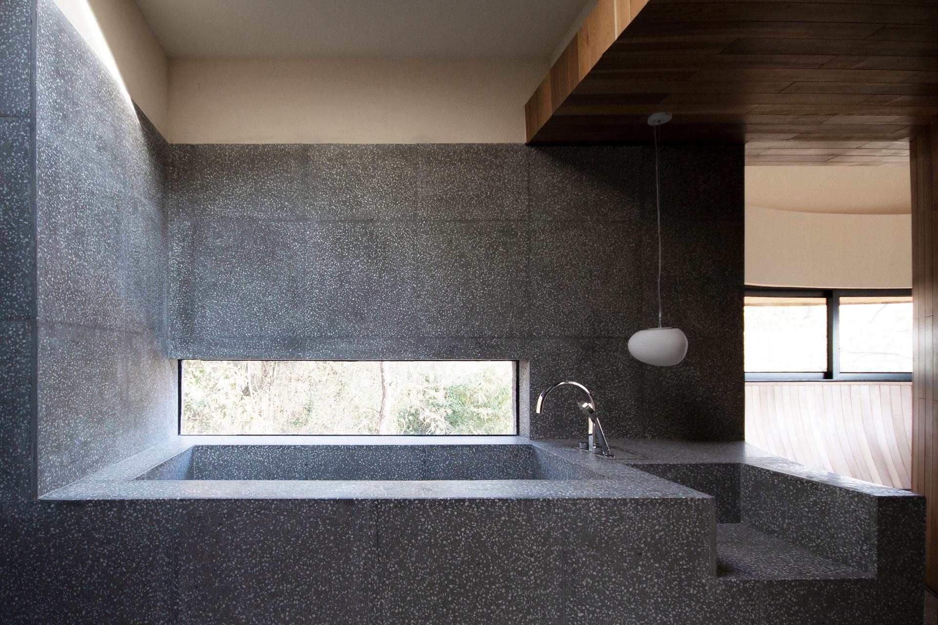 In this modern bathroom, there's a built-in bathtub with a horizontal window, which was designed to ensure privacy from the walking paths outside, while still allowing views of nature.
