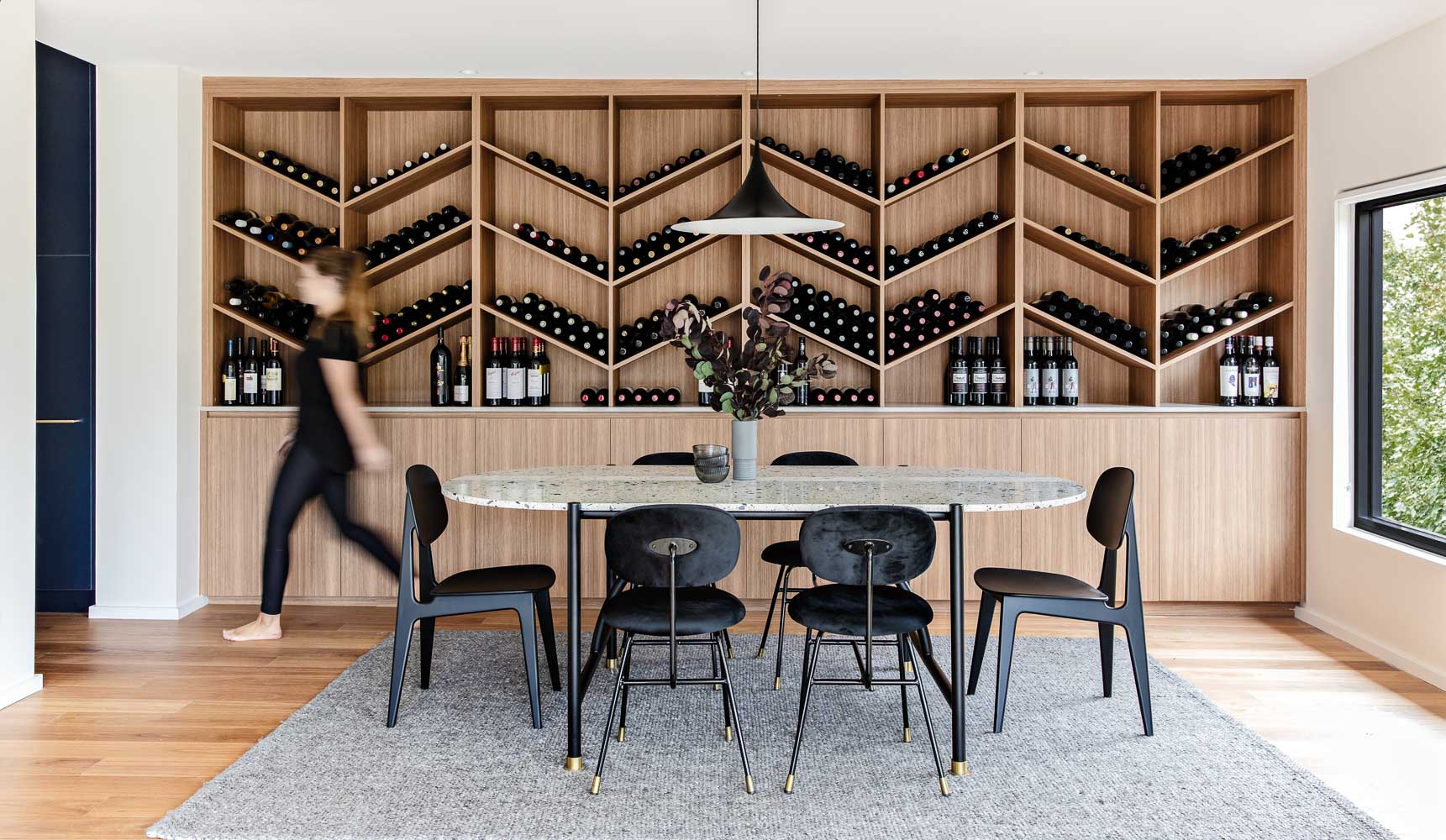 The wine storage wall, which is made from wood, includes lower cabinets, a countertop, and a shelving unit with a chevron design.