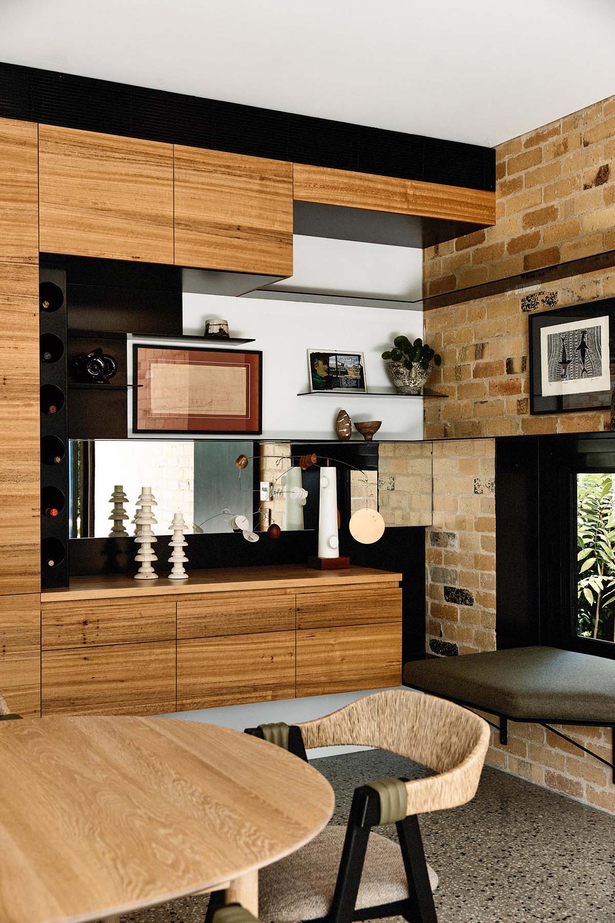 The wood cabinets from the kitchen continue through to this dining room, and result in an open niche with shelving. Beside the cabinets and in the brick wall, there's a small built-in window seat.