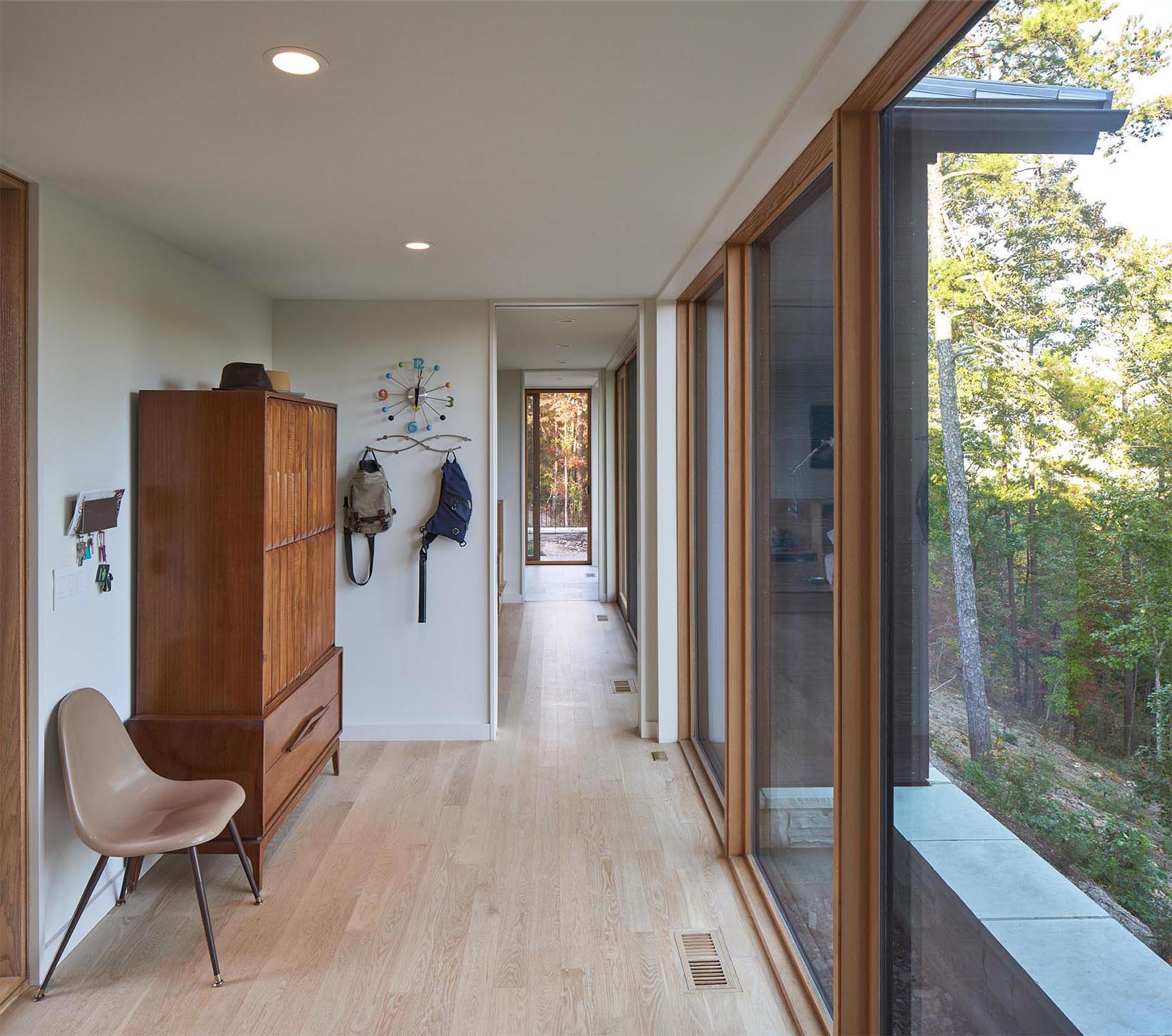 A modern hallway with large floor to ceiling windows that frame views of the trees, and create an abundance of natural light for the hallways.
