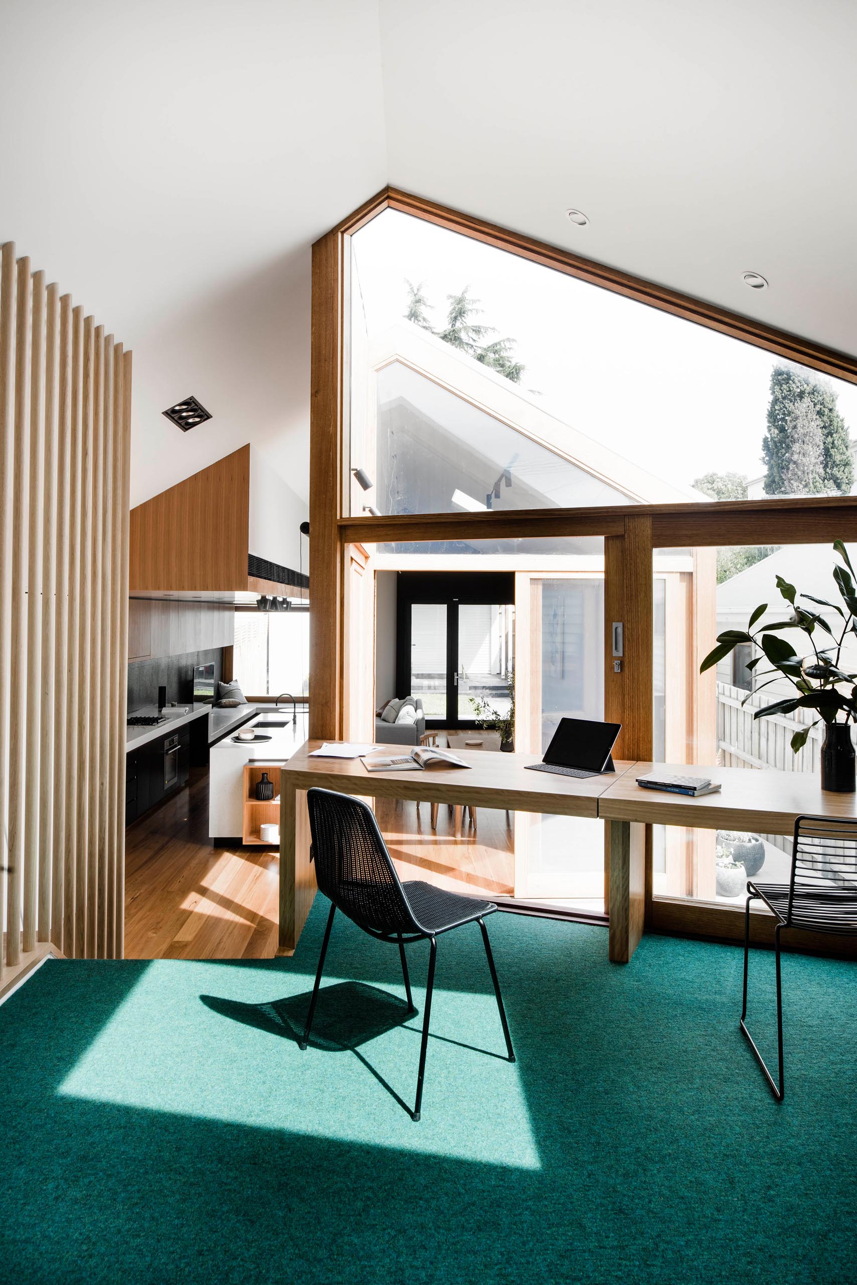 A modern house with a home office that has green carpet and a desk that lines the angled window and overlooks a small courtyard.