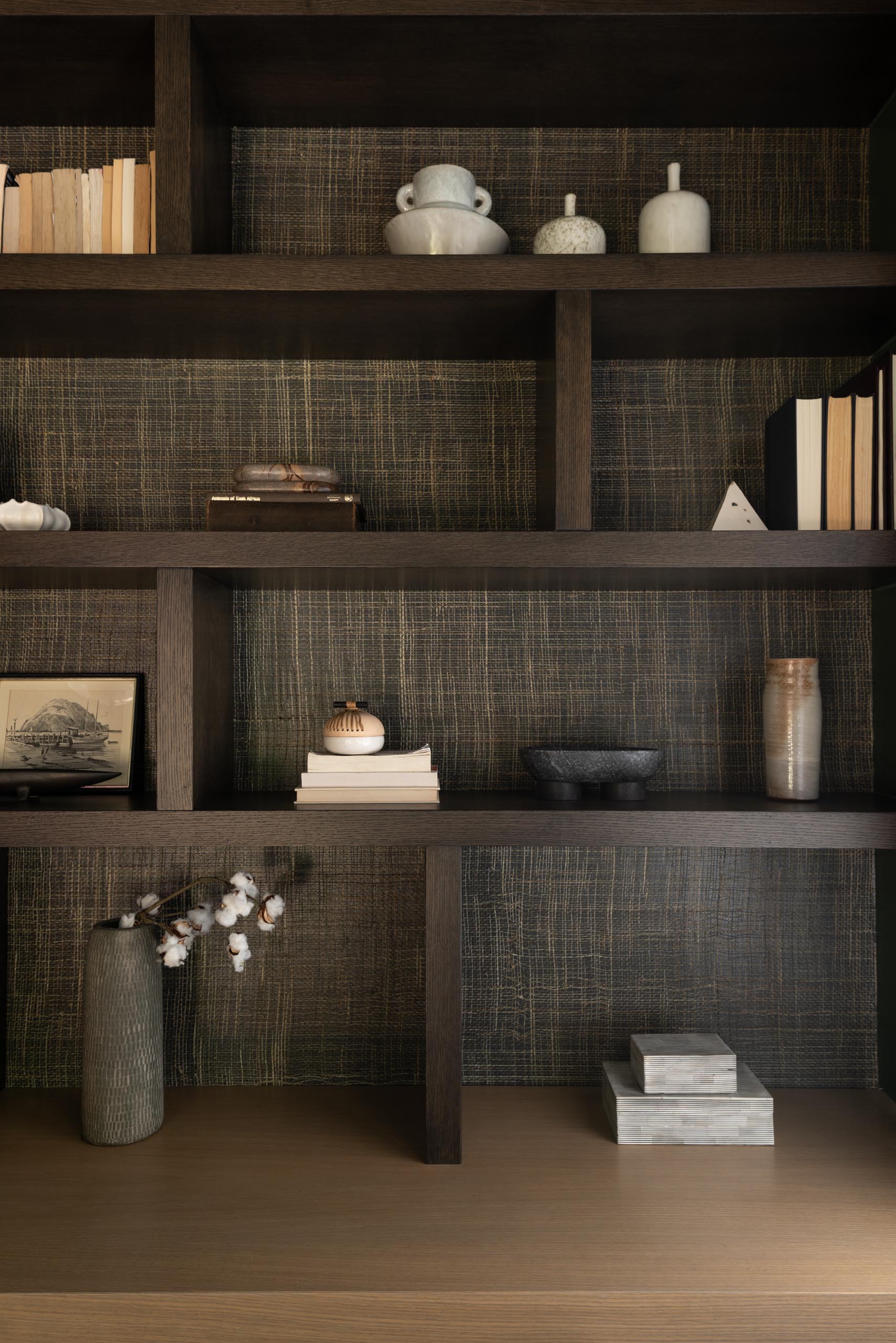 A modern and dramatic bookshelf includes a dark stain and a natural wallpaper backing.